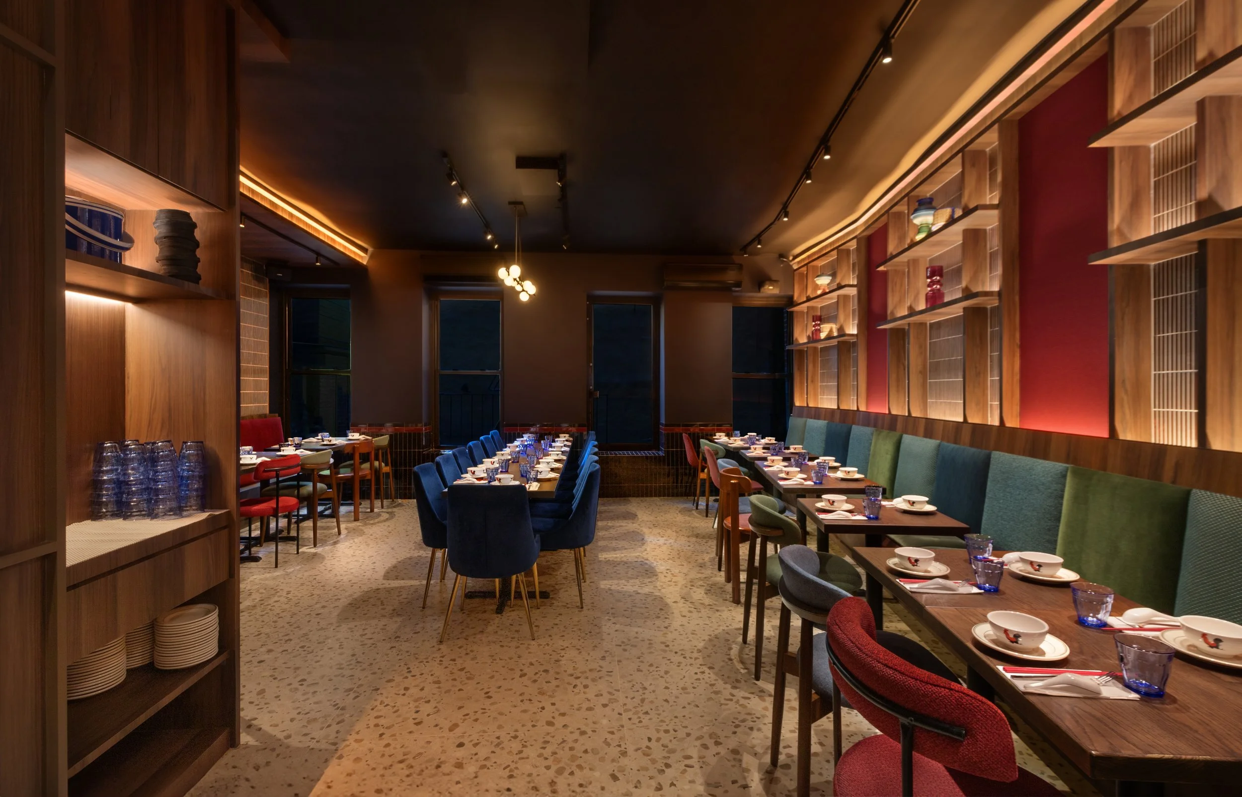 Elegant restaurant dining room with tables set with dishes, glasses, and utensils, features colorful seating, wooden shelves with decorative items, and warm lighting.