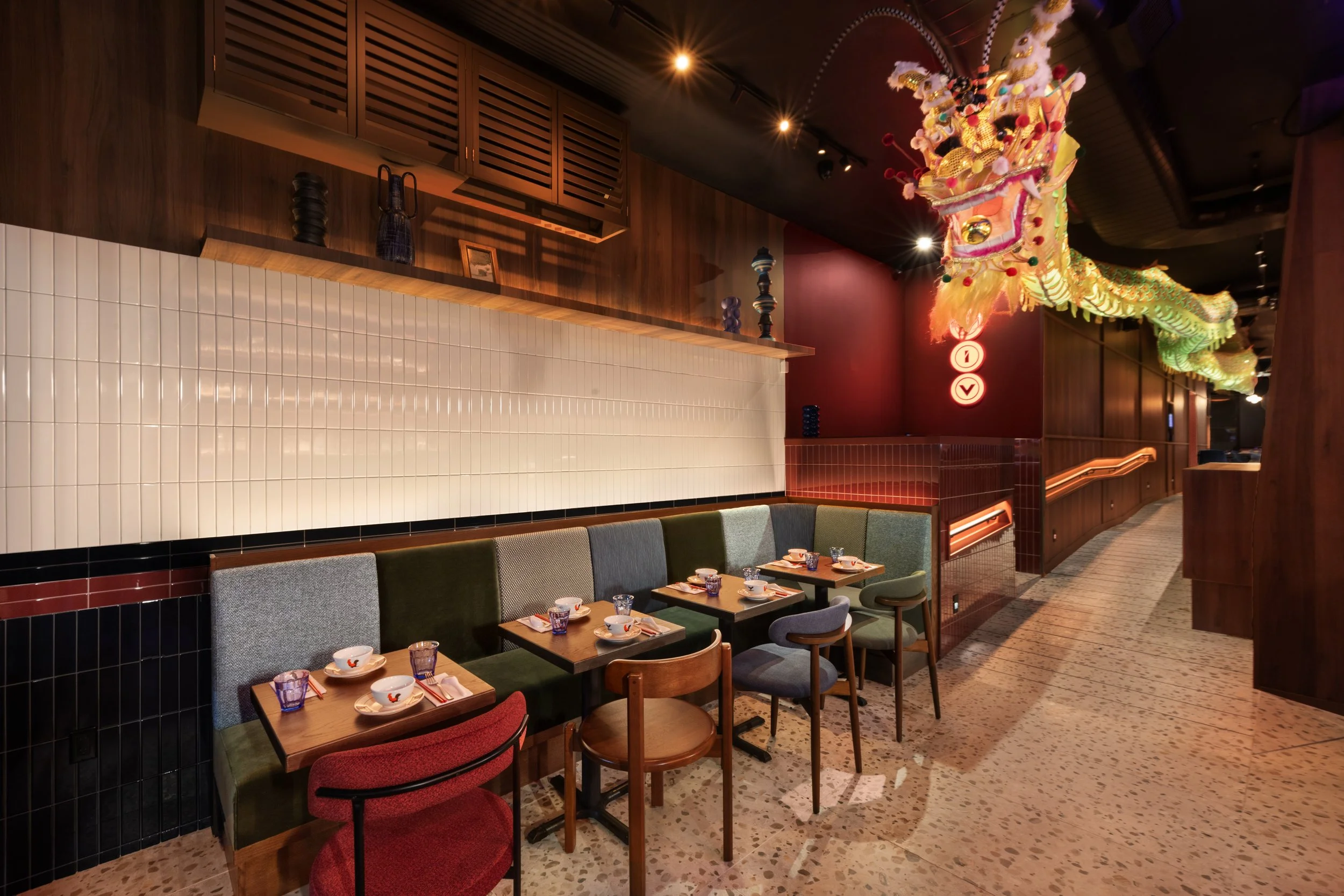Inside a restaurant with a dragon decoration hanging from the ceiling, set up for dining with small plates, glasses, and utensils on tables, wooden and tiled decor, with warm lighting.