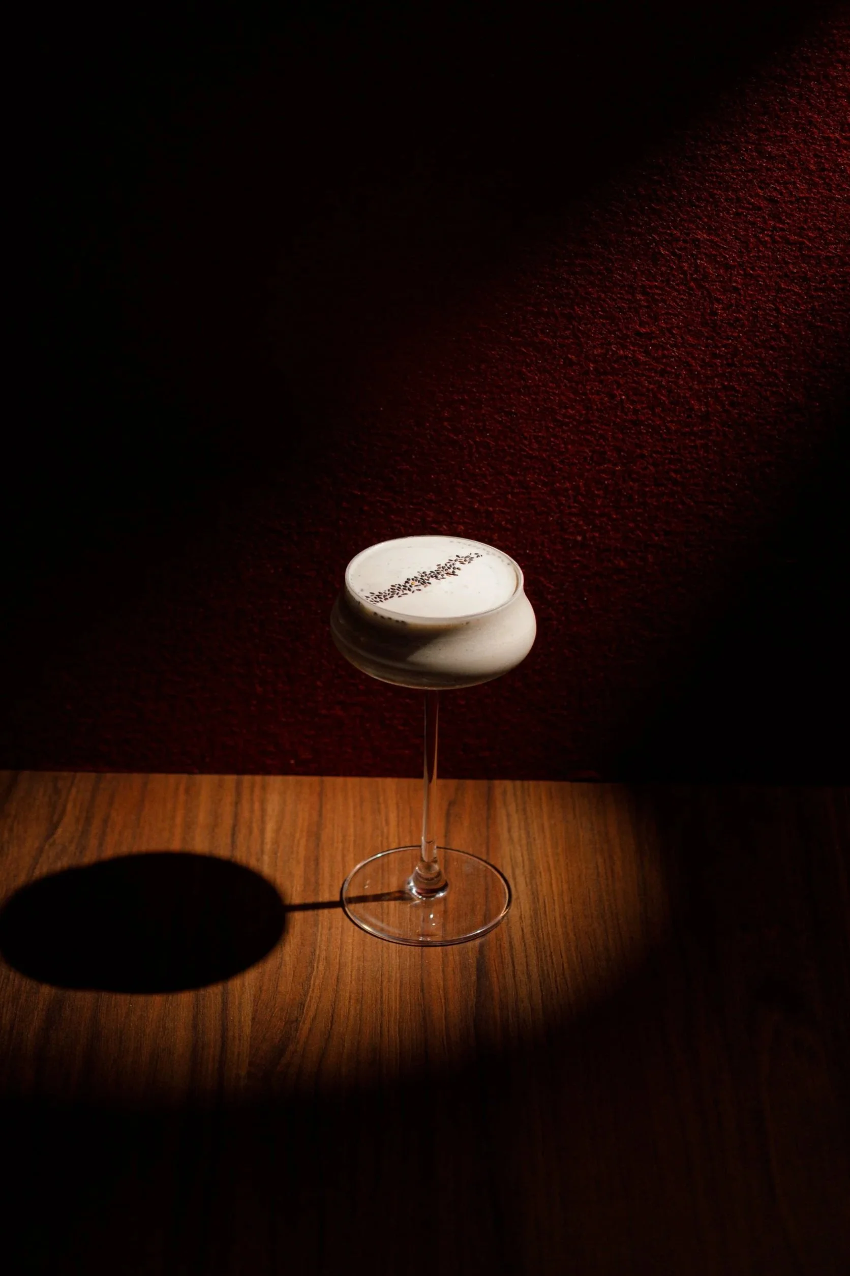 A white ceramic bowl on top of a tall, clear glass stand, with text written inside the bowl, placed on a wooden floor against a textured red wall.