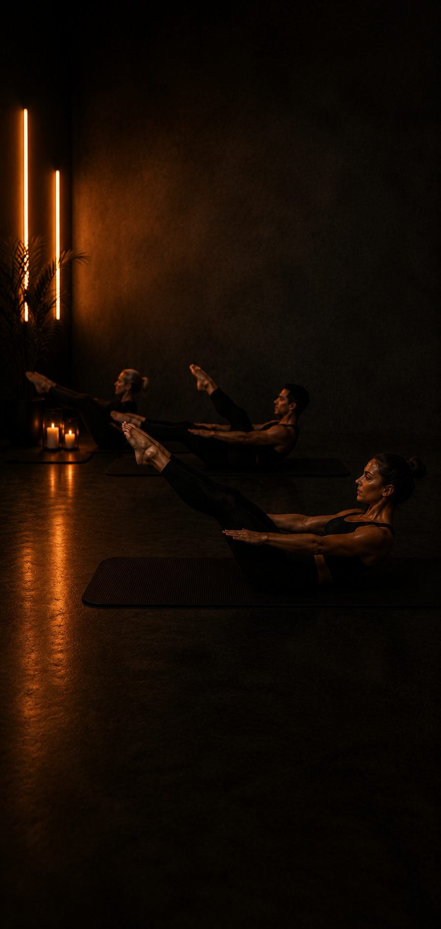 Three women participating in a yoga/pilates class, performing boat pose on yoga mats in a dimly lit room with candles and decorative lights.