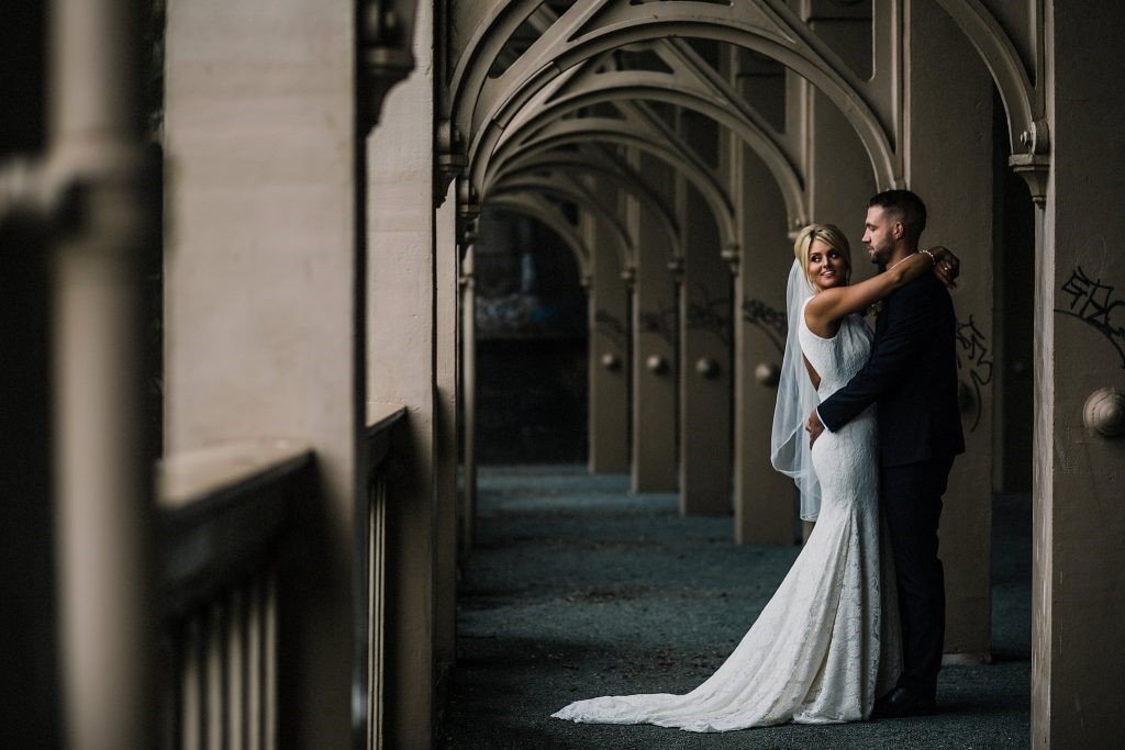 Bride and groom embracing under an arched, outdoor walkway at night.