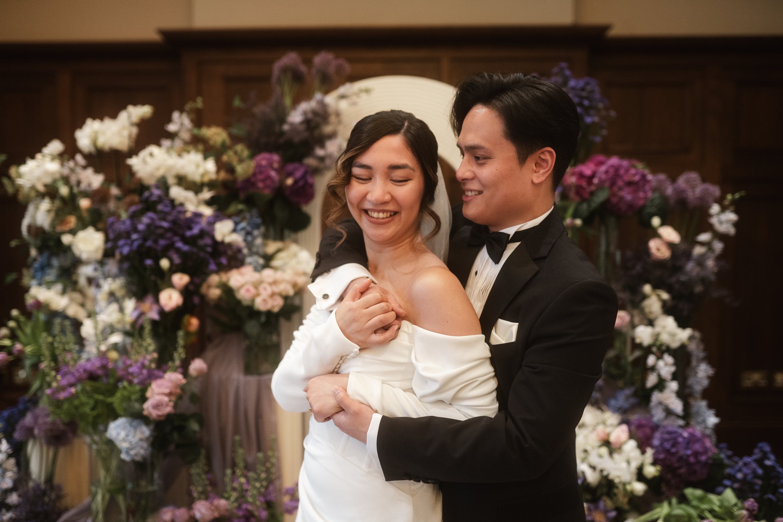 A bride and groom dancing in front of a backdrop of colorful flowers at their wedding reception.