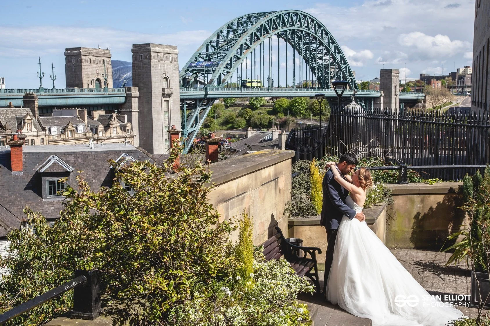 A bride and groom embrace on a rooftop with the Sydney Harbour Bridge in the background.