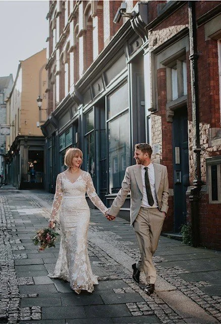 A bride and groom holding hands and walking down a city street during their wedding.