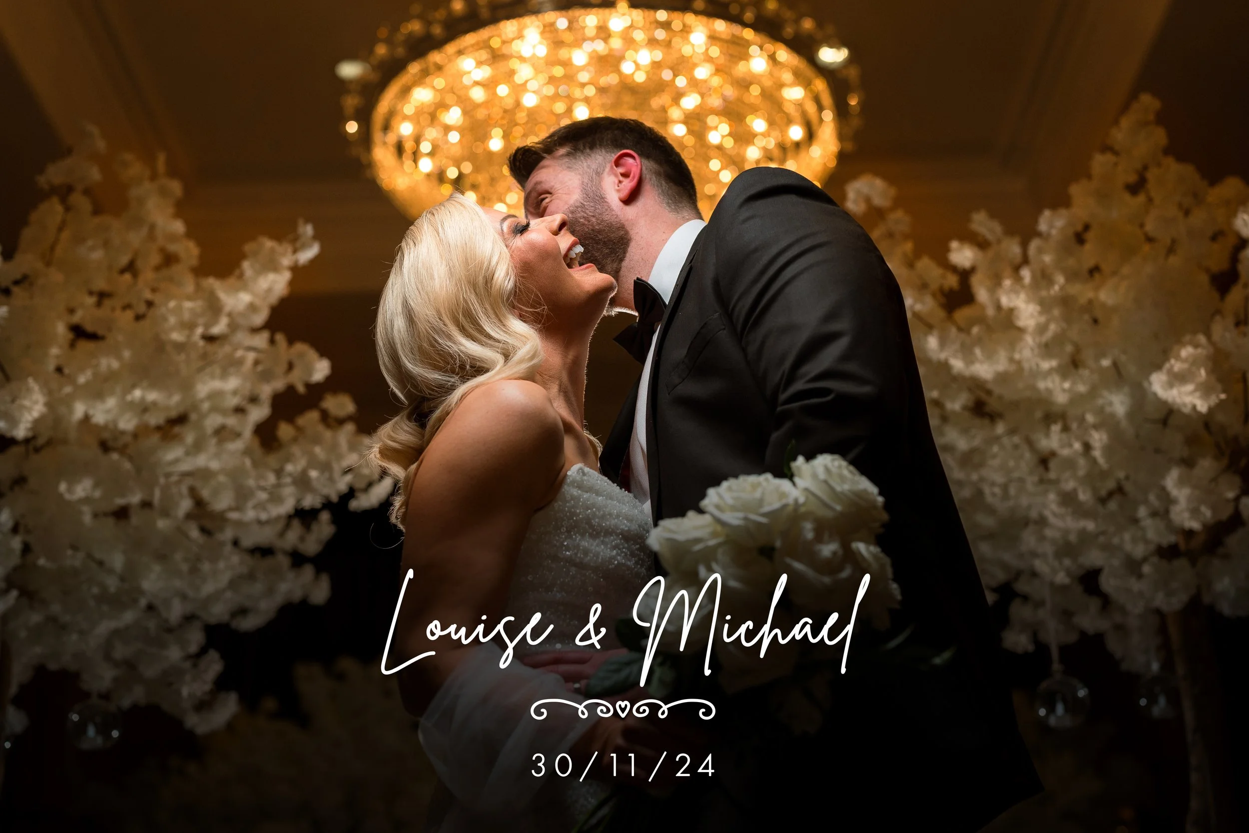 A bride and groom share a kiss at their wedding reception, with a chandelier overhead and floral decorations around them. The image includes text with the names Louise and Michael and the date 30/11/24.