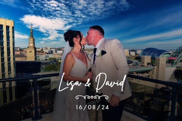 A bride and groom kissing on a balcony with a city skyline, including a tall church spire, in the background. The text overlays say "Lisa & David" and the date "16/08/24".