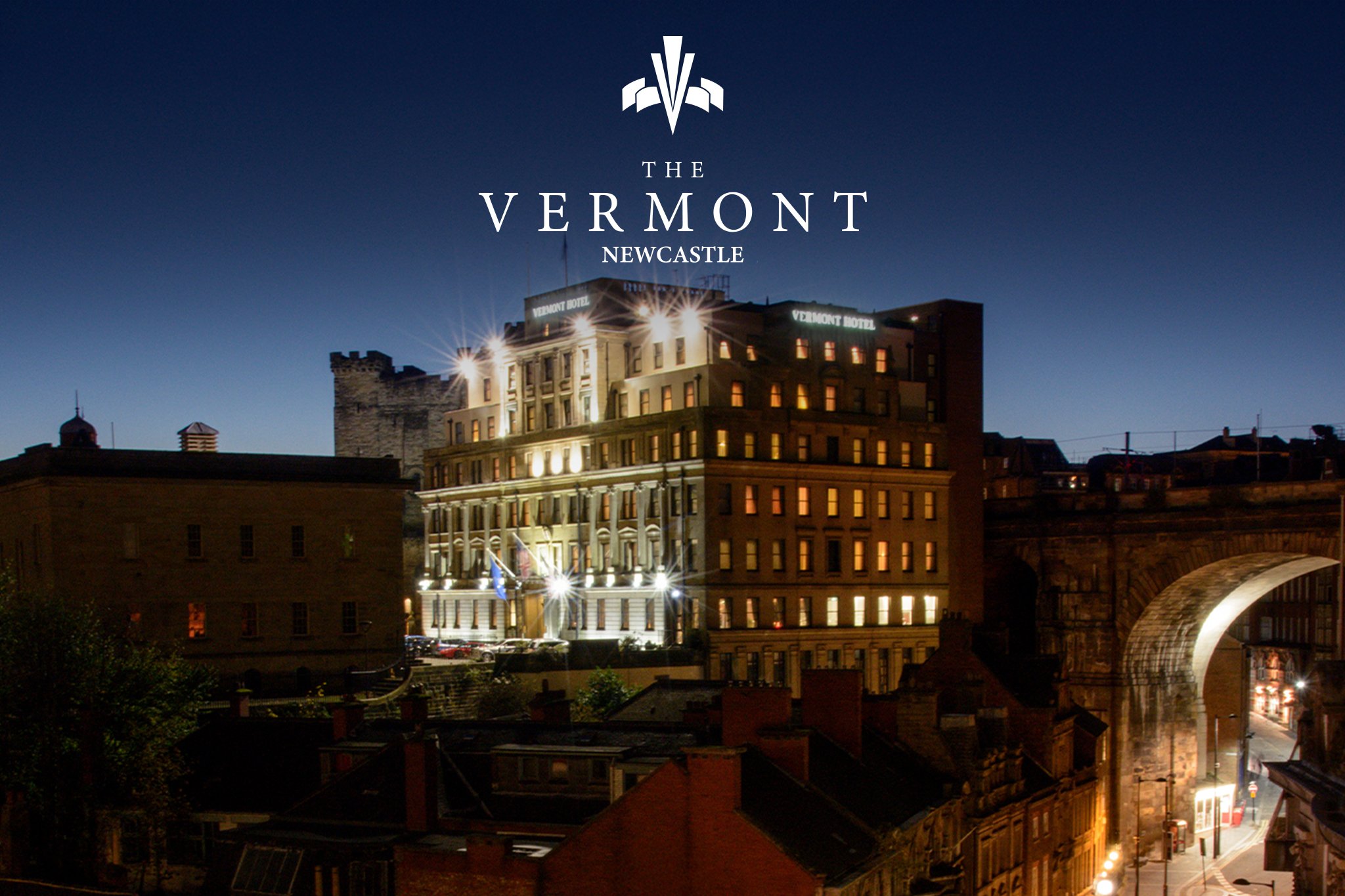 Nighttime view of a historic hotel building with illuminated signs reading 'Vermont Hotel' on a city street in Newcastle, Vermont, with a dark sky and surrounding buildings.