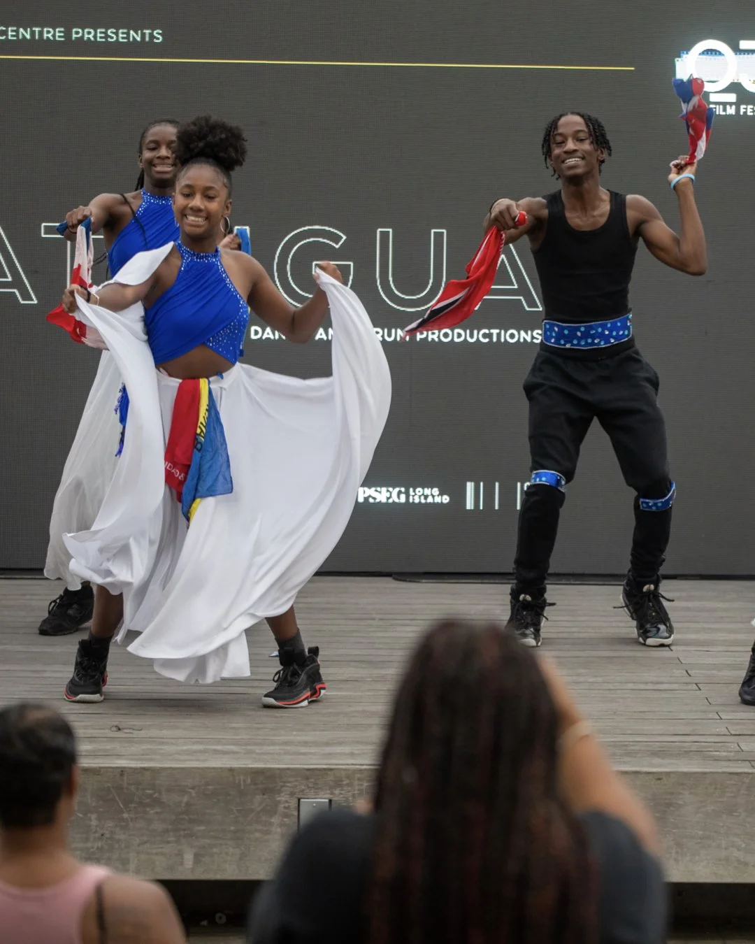 Four young dancers on stage, two girls in blue costumes and two boys in black costumes, performing with energetic dance moves, during an event at a film festival.