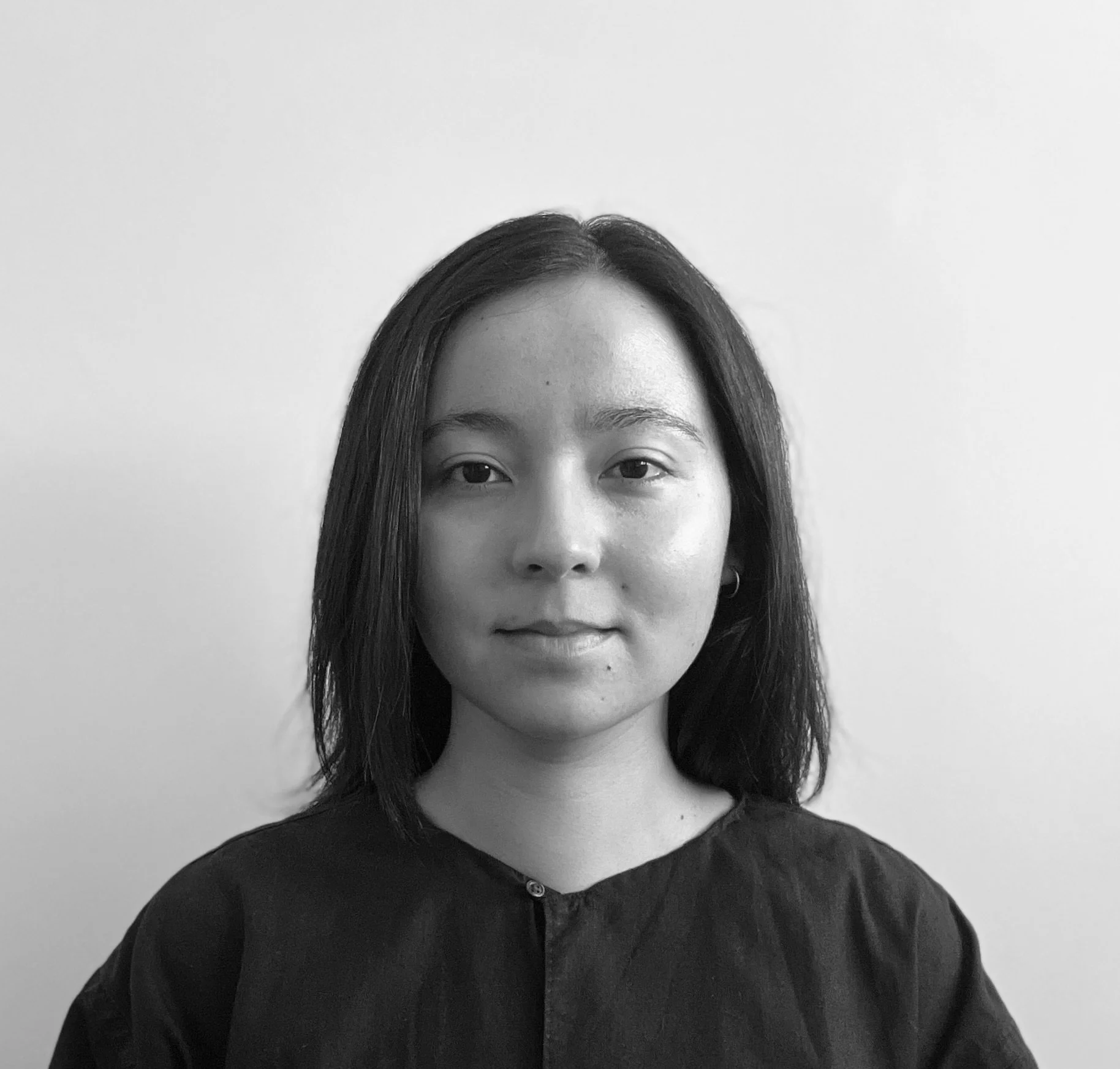 A young woman with straight, shoulder-length hair, wearing a dark top, looking directly at the camera, in front of a plain light-colored background.