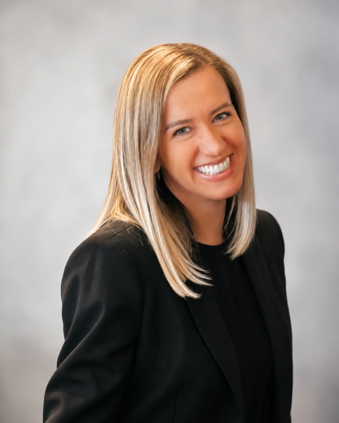 A woman with shoulder-length blonde hair smiling at the camera, wearing a black blazer.