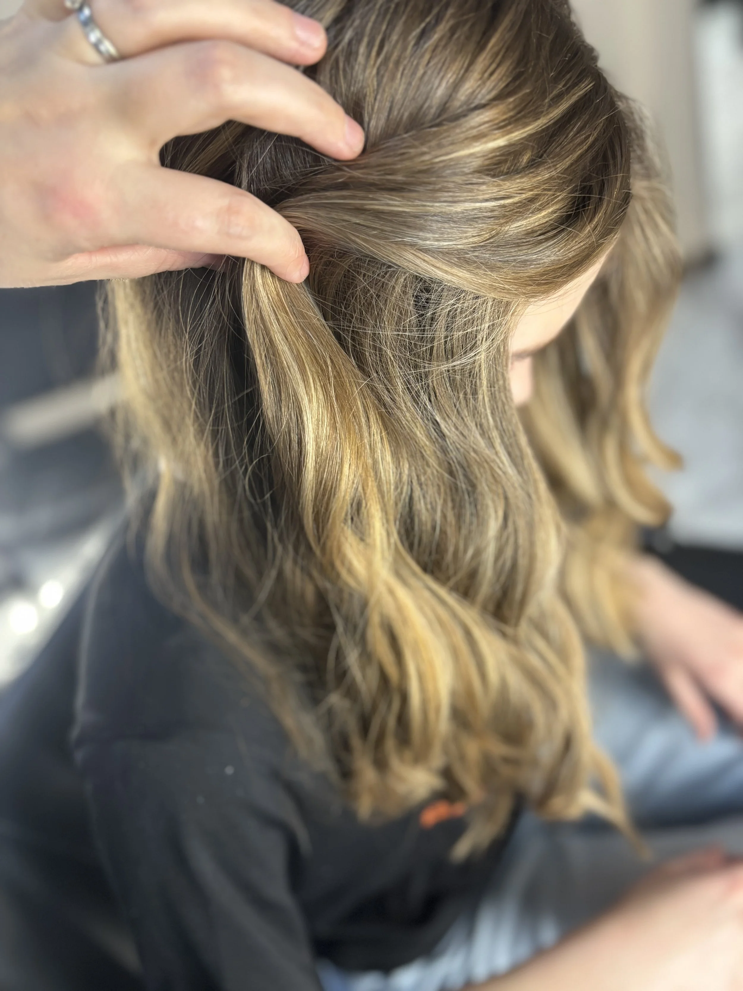 A person with blonde, wavy hair, receiving a massage on their scalp in a salon or spa setting.