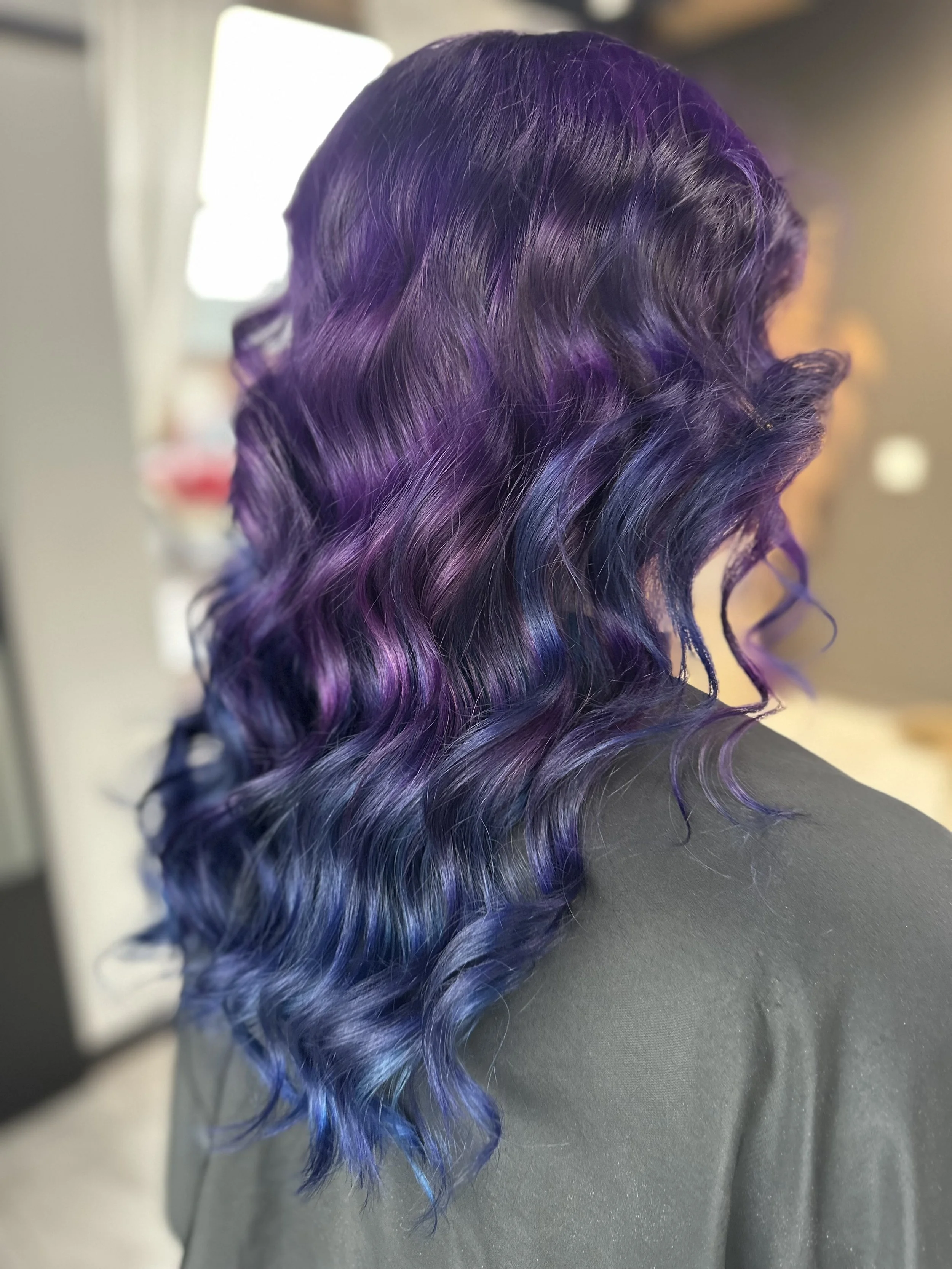 Side view of a person's head with wavy hair dyed purple and blue.