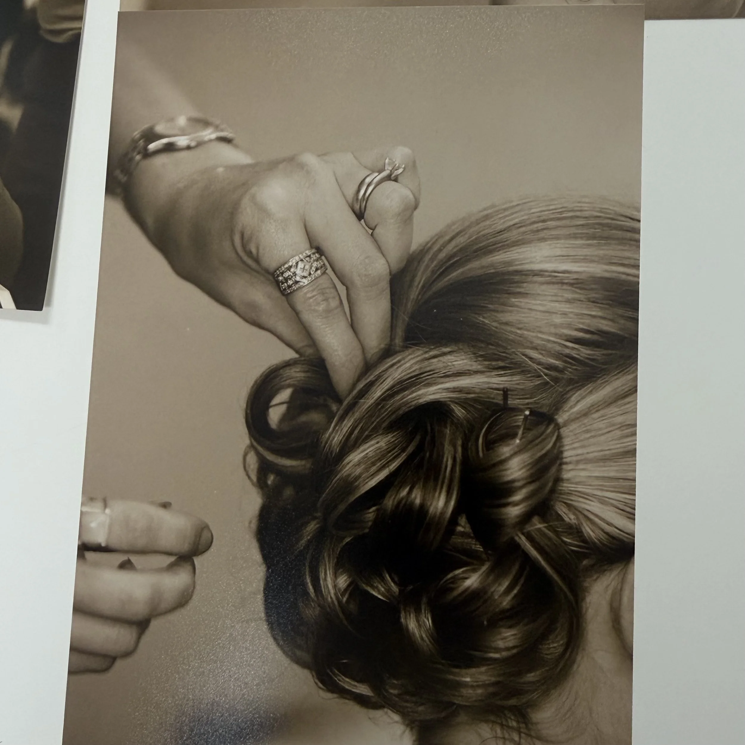 A black and white photo of a woman with long hair, wearing jewelry, holding her hand up near her face.