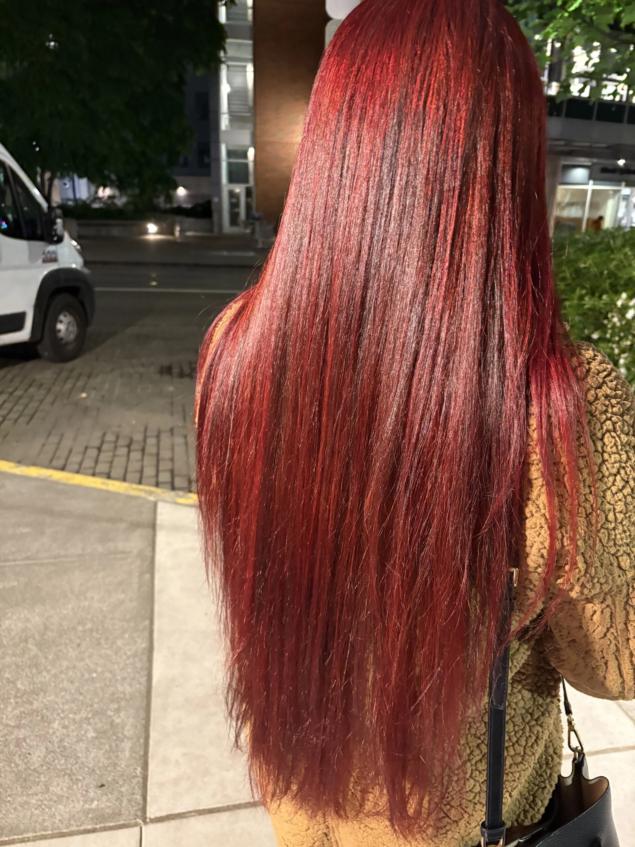 Person with long, straight, shiny red hair standing outdoors at night.