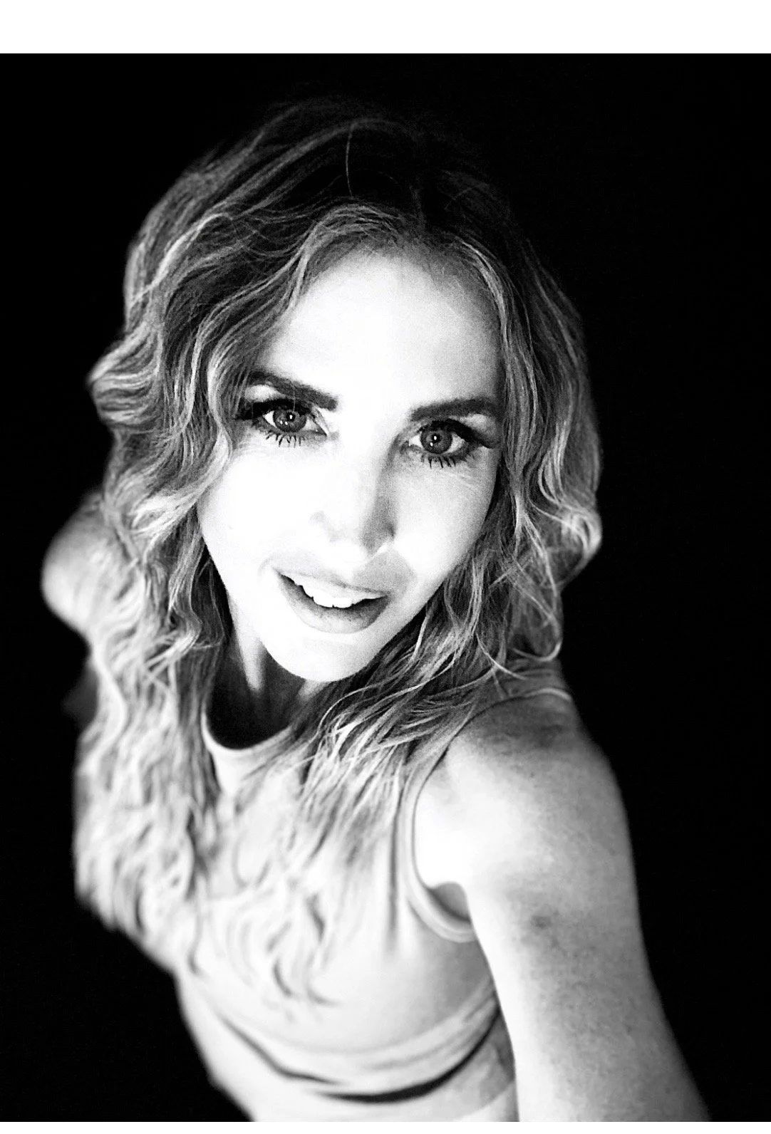 Black and white close-up photo of a woman with wavy hair smiling at the camera.