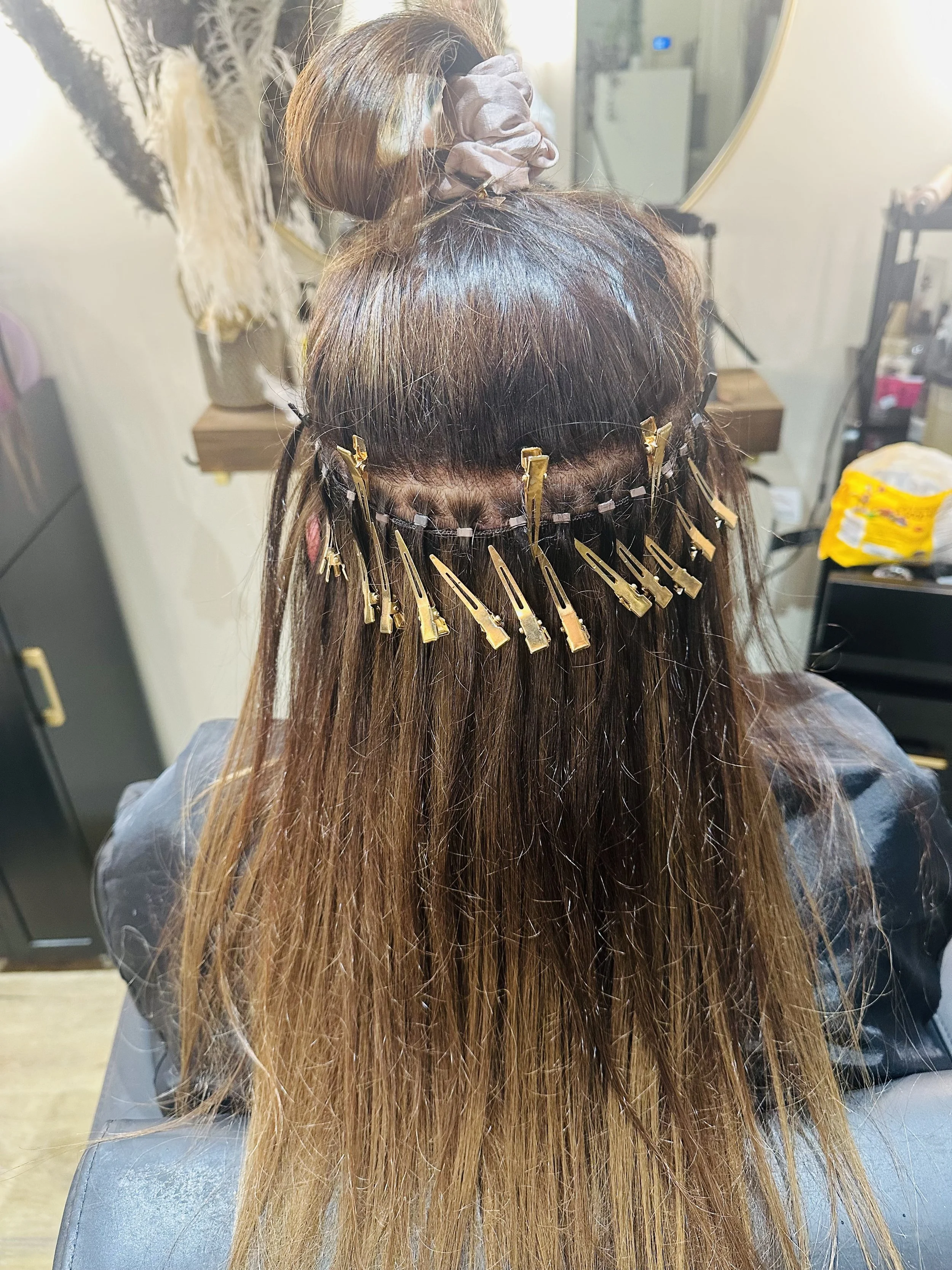 A person undergoing hair treatment with hair clips sectioning the long brown hair, sitting in a salon chair.