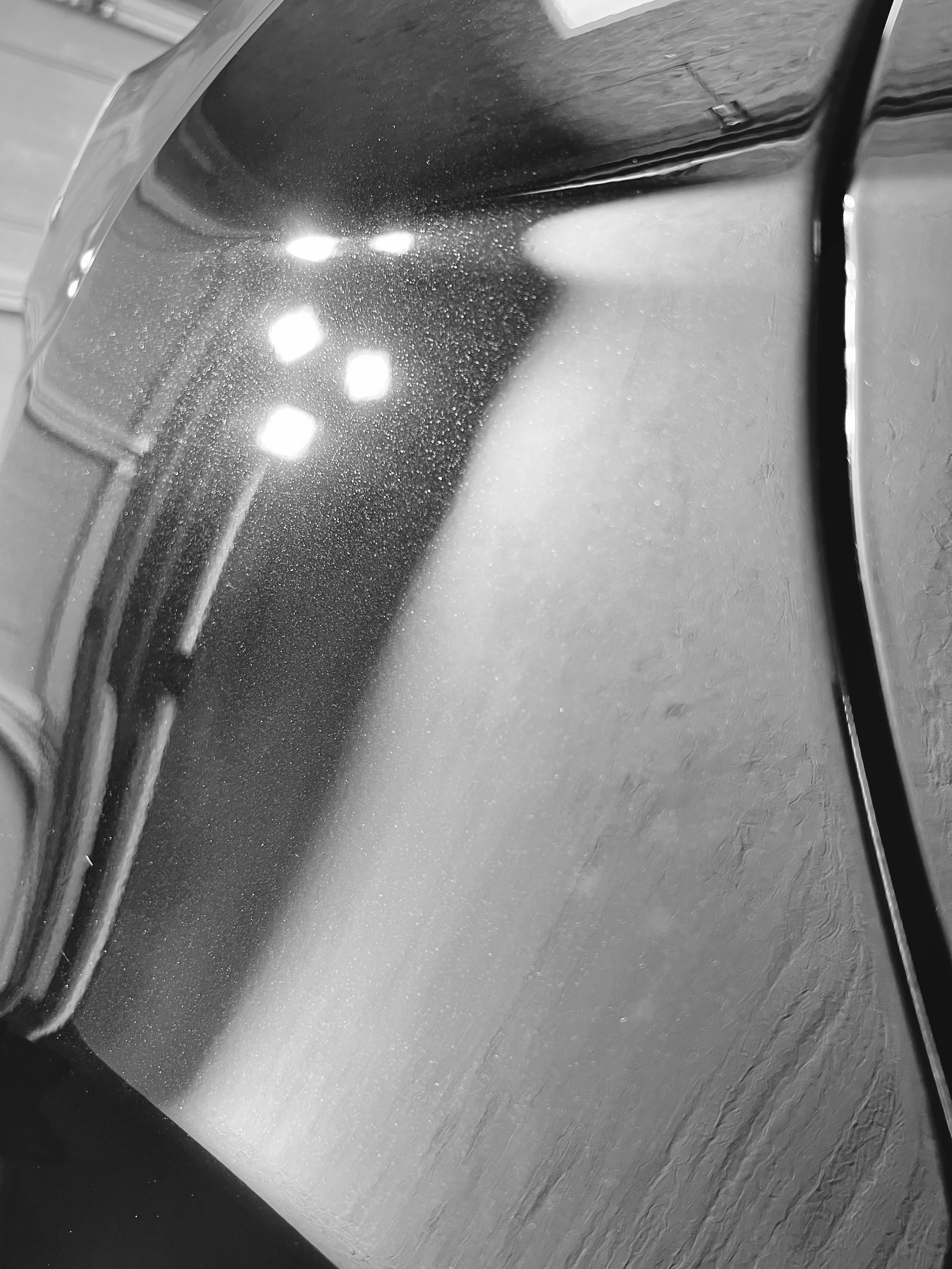 Ein schwarzer Ofen mit Glastür, der in einer Küche steht. Die Oberfläche des Ofens ist glänzend und reflektiert Lichtquellen. Das Bild ist in Schwarzweiß.