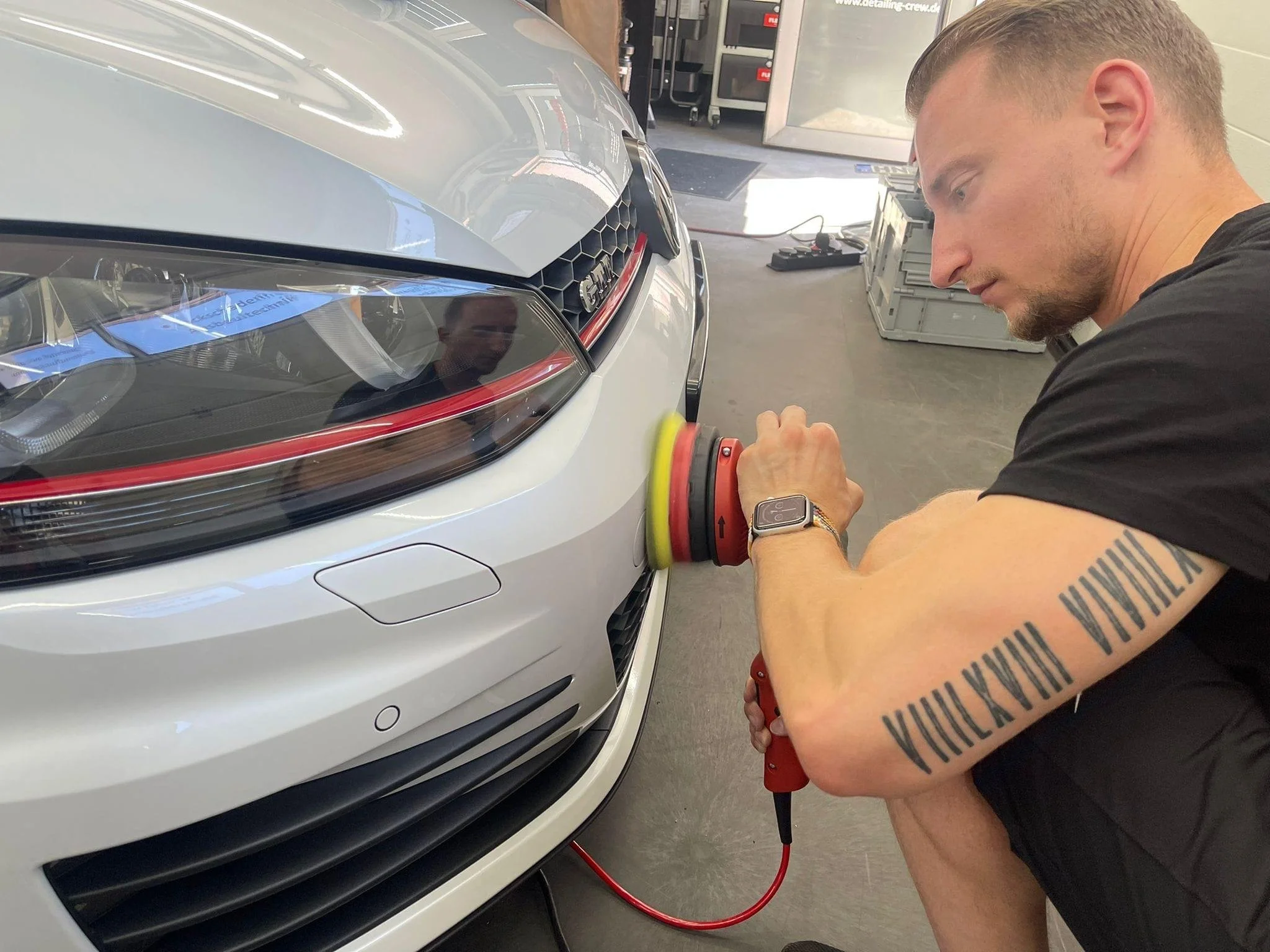 Michael poliert die Vorderseite eines Golf 7 GTI in der Halle, während er einen Exzenterschleifer benutzt.