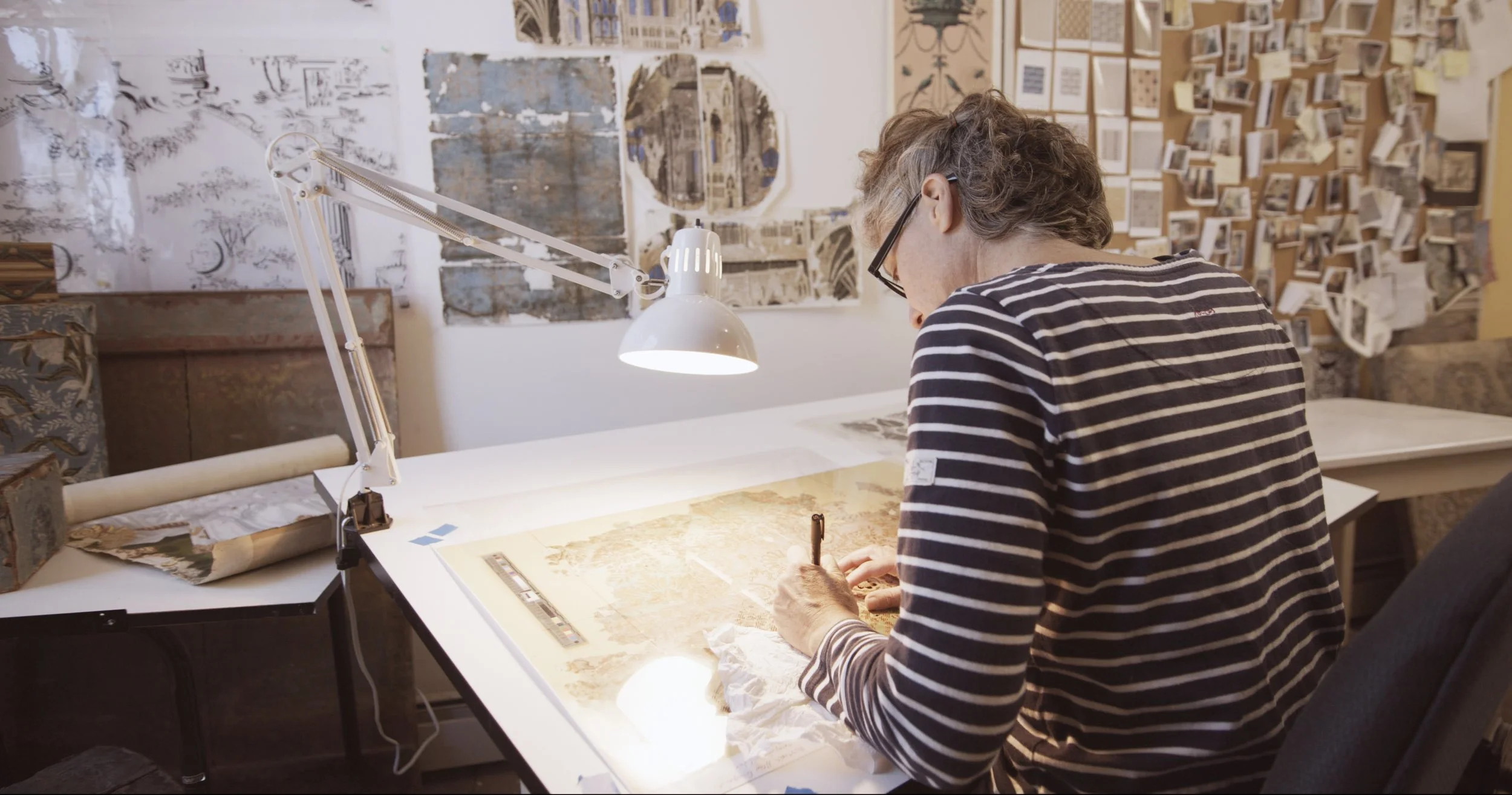 Michele drafting a historic wallpaper pattern from archival documents at the Adelphi Paper Hangings studio. The design is prepared on a transparency before being laser-cut onto printing blocks.