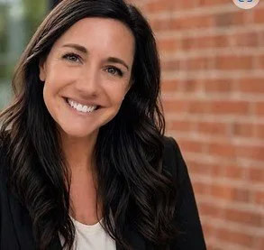 A woman with long dark hair smiling in front of a brick wall