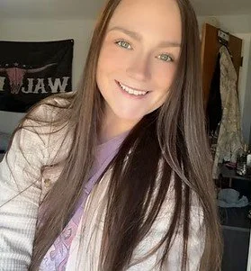 Smiling young woman with long brown hair taking a selfie indoors.