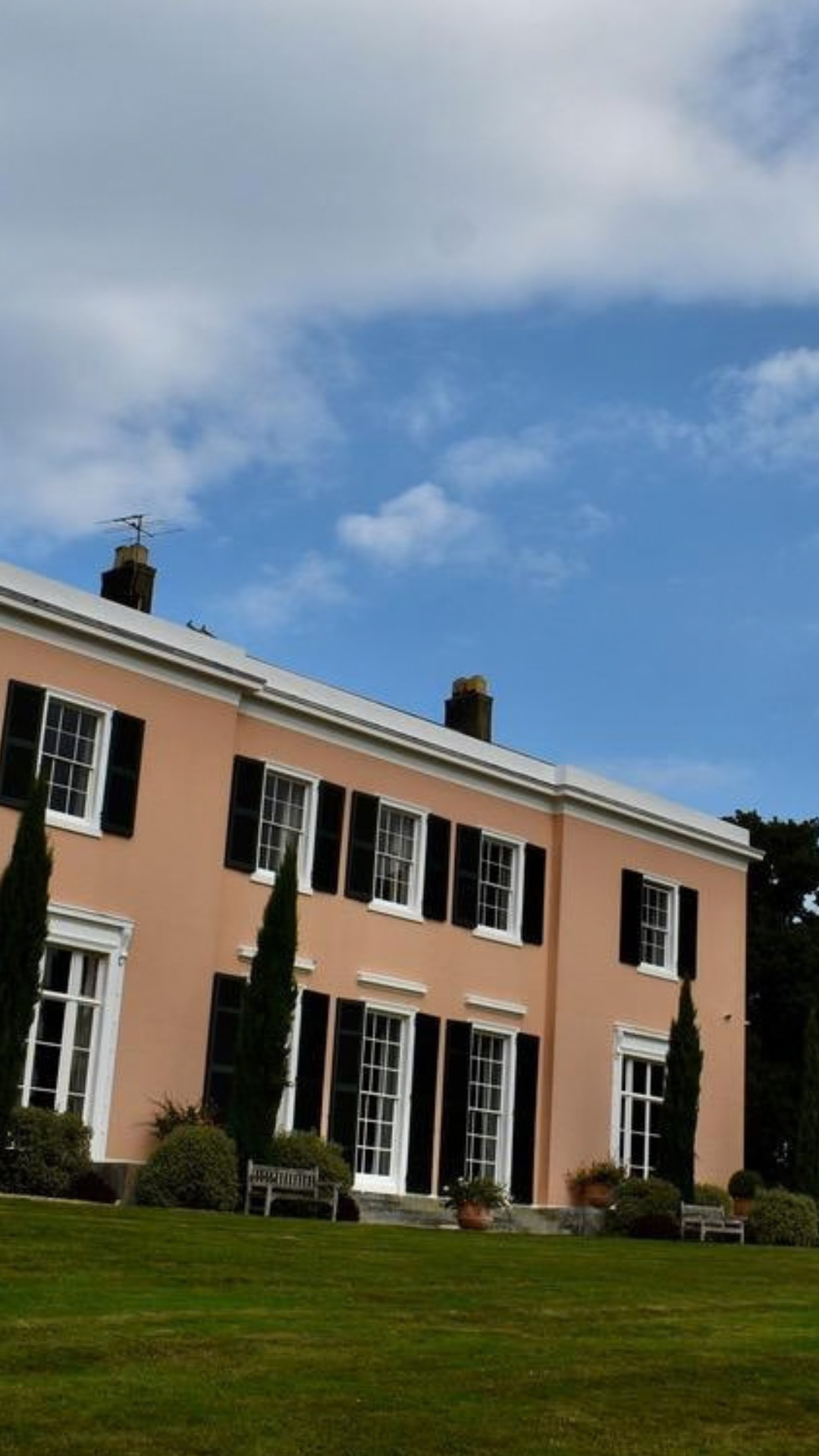 Peach-colored Georgian-style mansion with black shutters, manicured lawn, and blue sky
