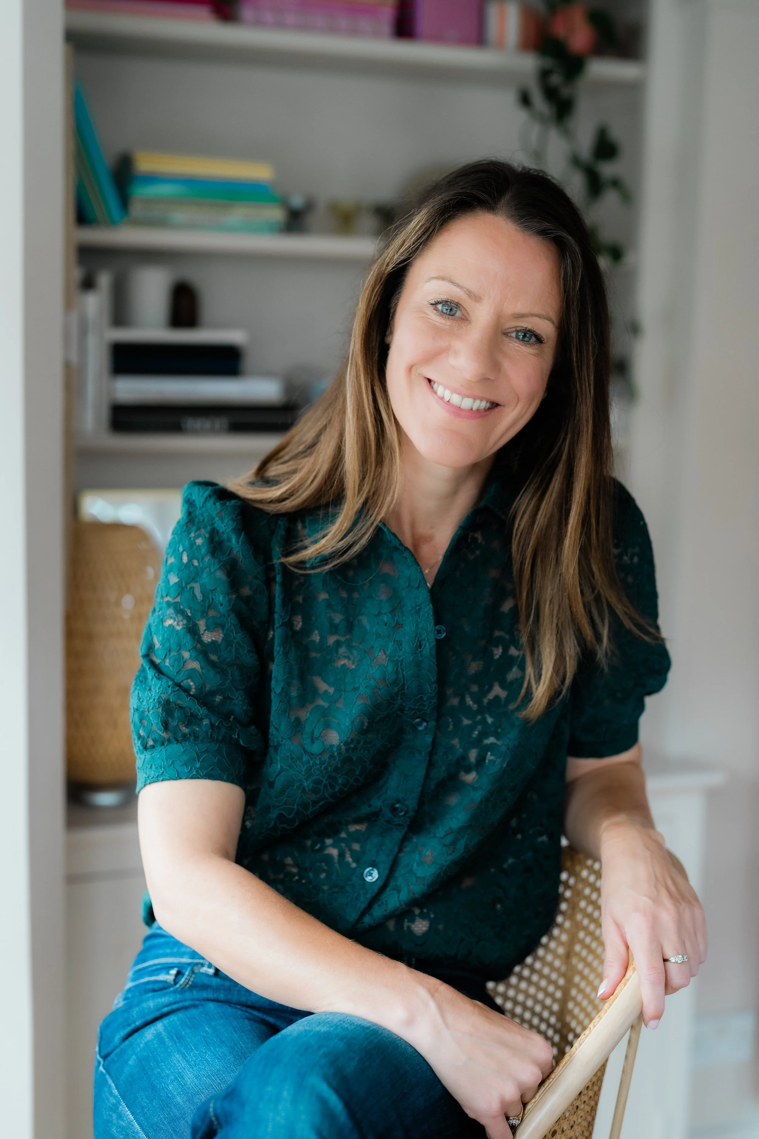 Smiling woman in a teal lace blouse sitting in a wicker chair at home