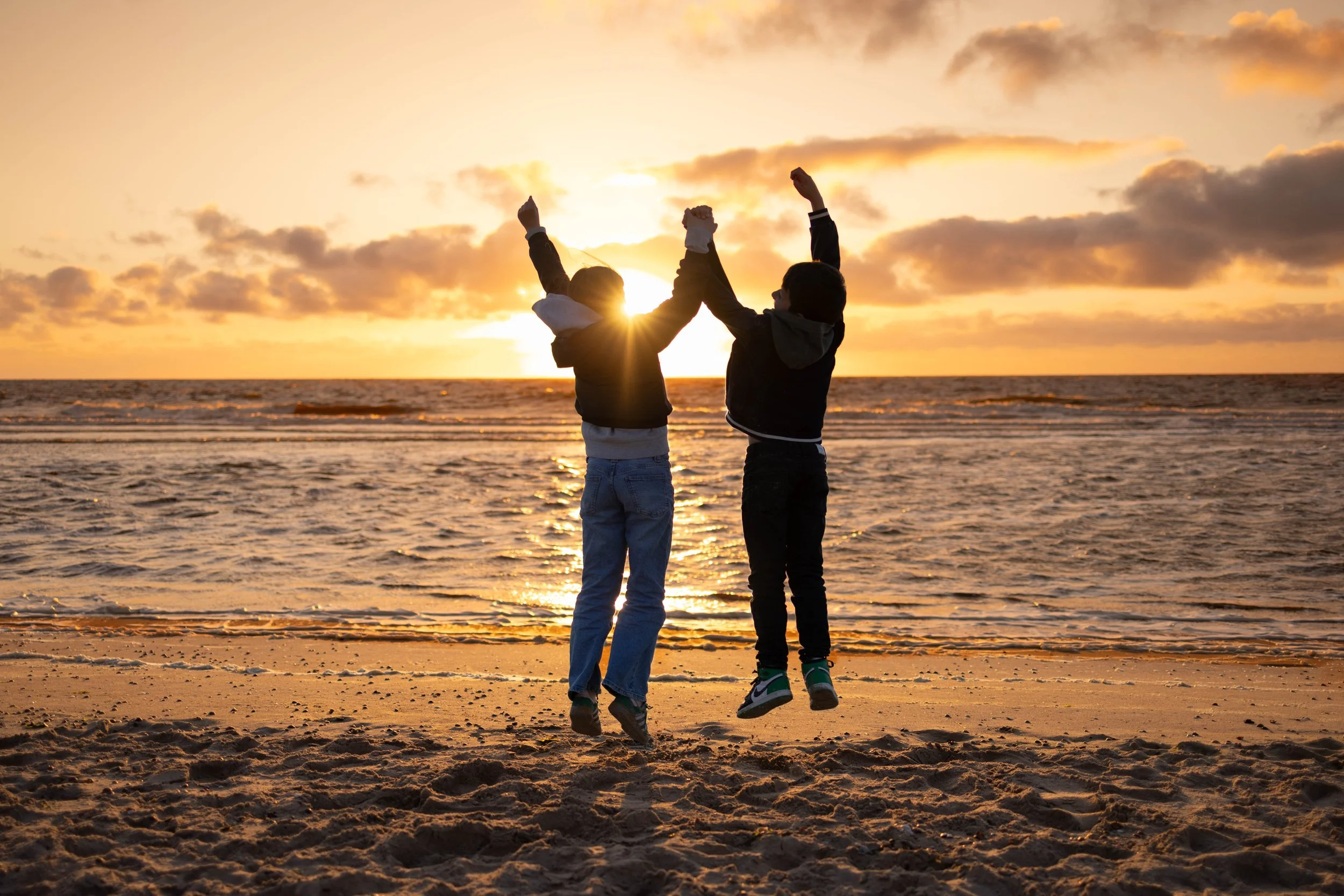 Zwei Jungen am Strand bei Sonnenuntergang, die sich hochfünfhaben.