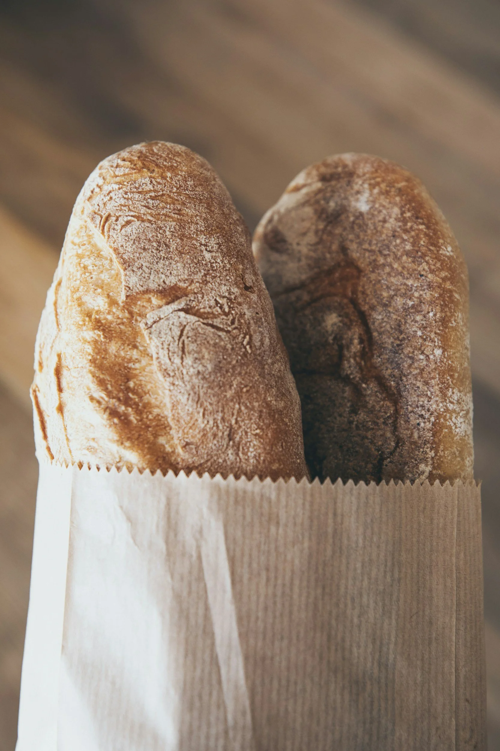 Two breadsticks in a paper bag, resting on a wooden surface.