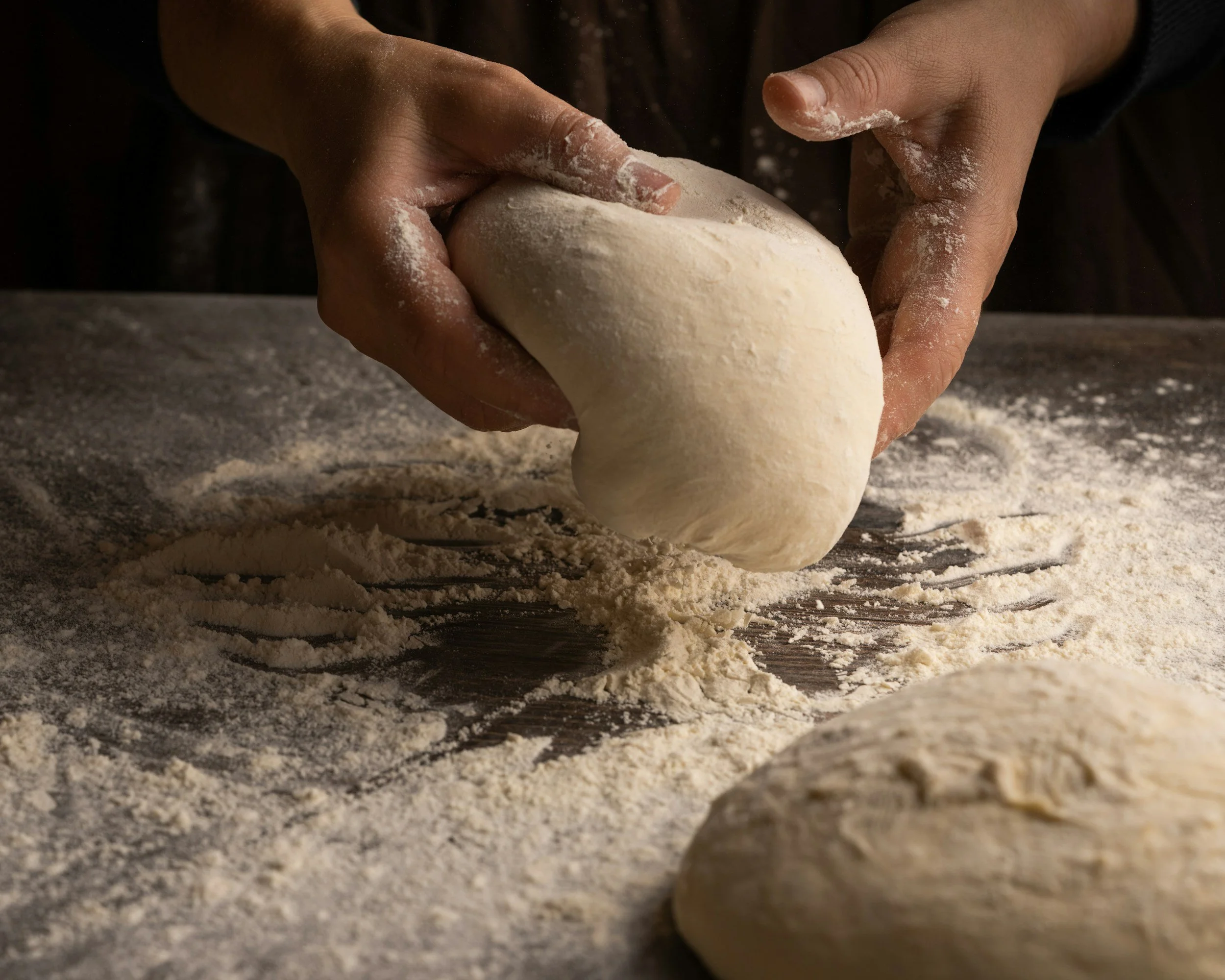 Hands kneading dough on a floured surface.