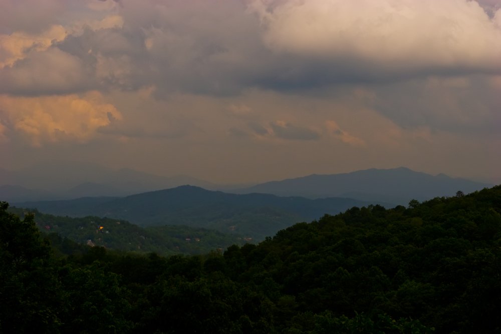 Landscape of rolling hills and mountains under a cloudy sky at sunset or dusk.
