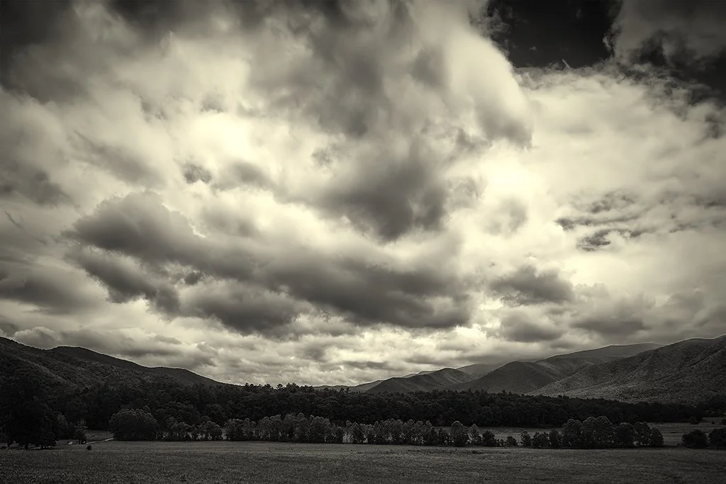 A landscape scene with dark, cloudy skies over rolling hills and a grassy field.