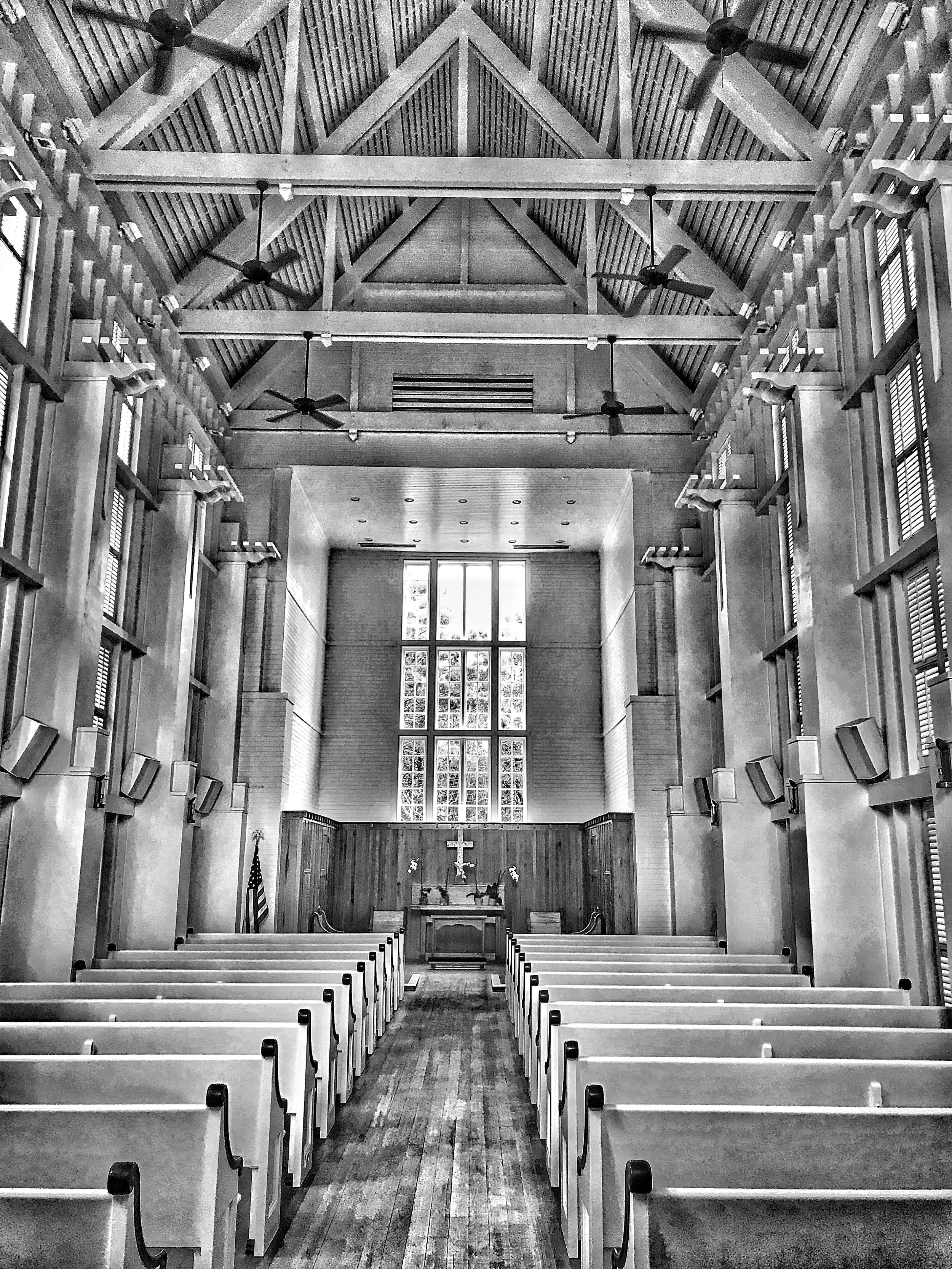 Interior of a church with wooden pews, large window at the front, crucifix on the wall, and American flag on the left side.