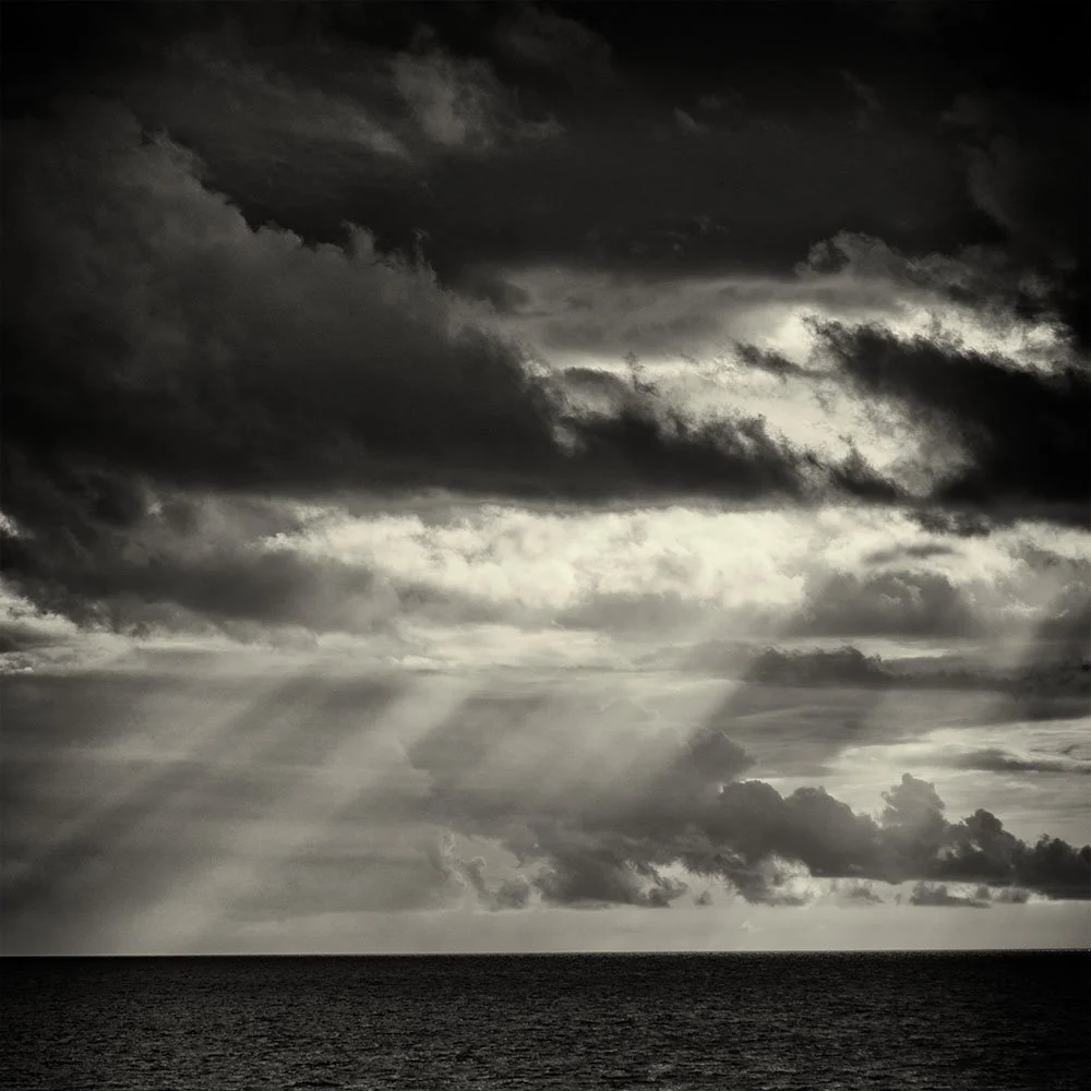 Dark and cloudy sky over the ocean with rays of sunlight breaking through the clouds.