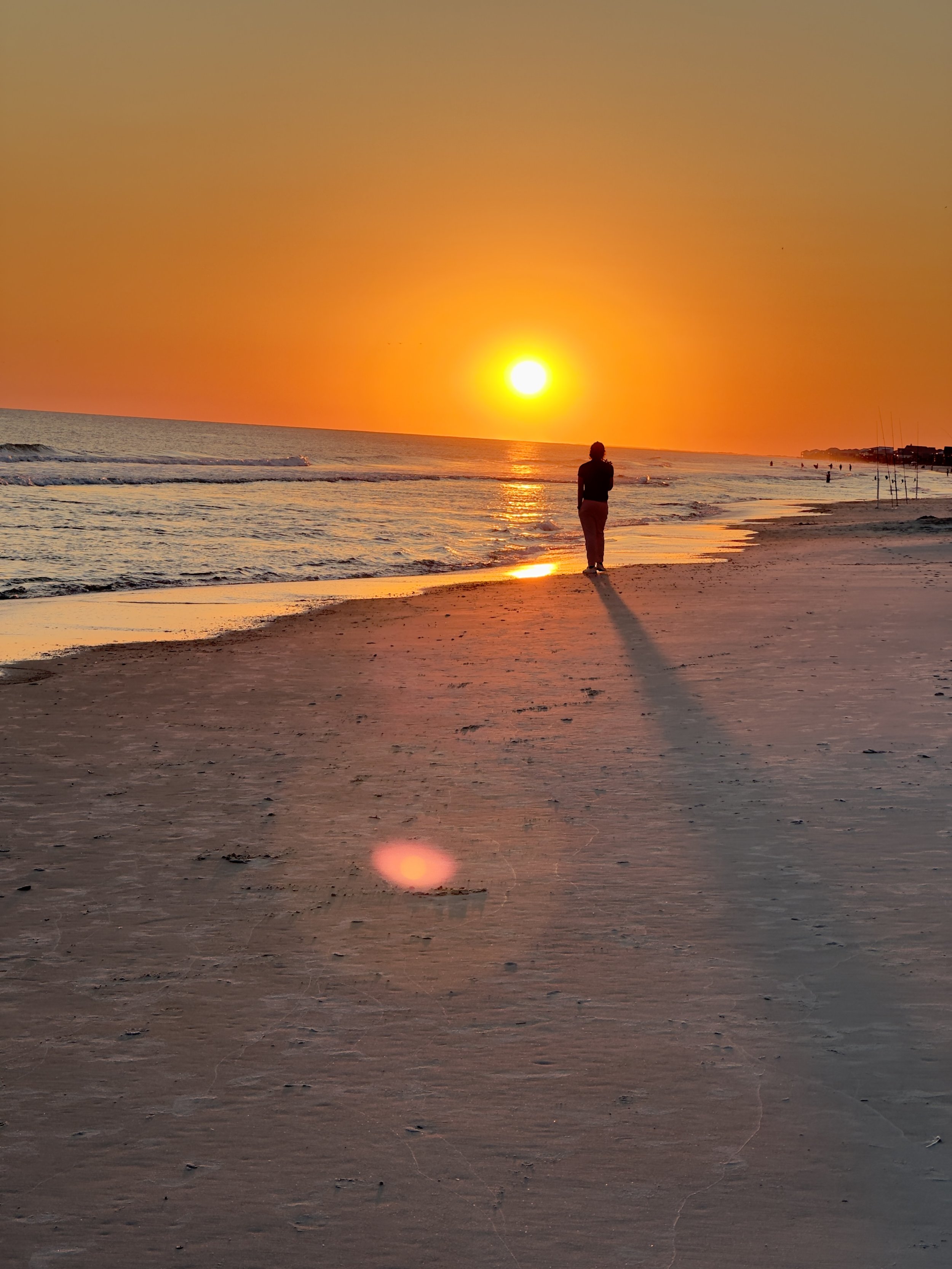 A person standing on a sandy beach watching the sunset over the ocean.