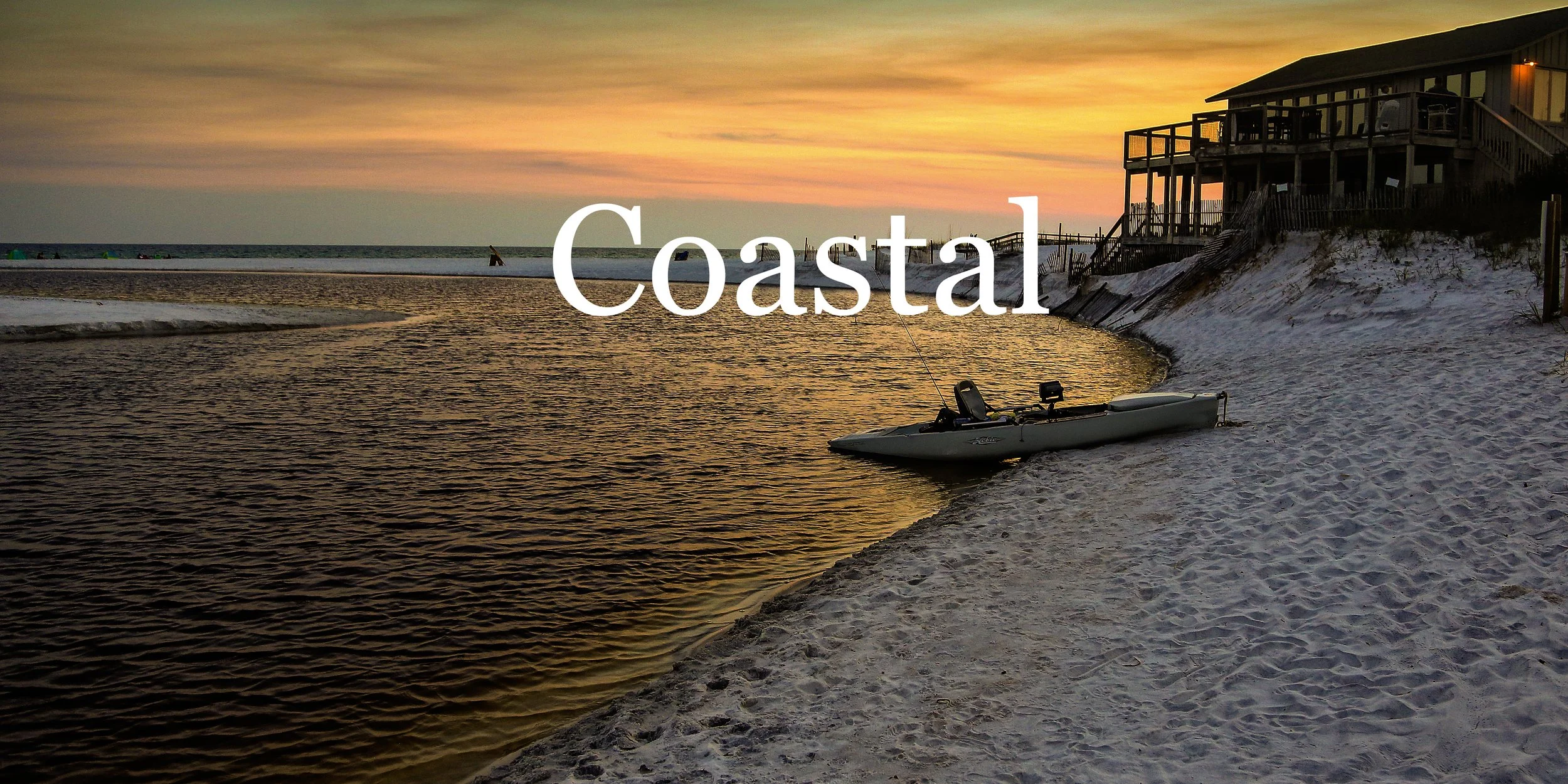 A coastal scene at sunset with a sandy beach, a kayak on the shore, and a house on stilts above the dunes. The sky has pastel hues of orange, yellow, and purple, reflecting on the water.