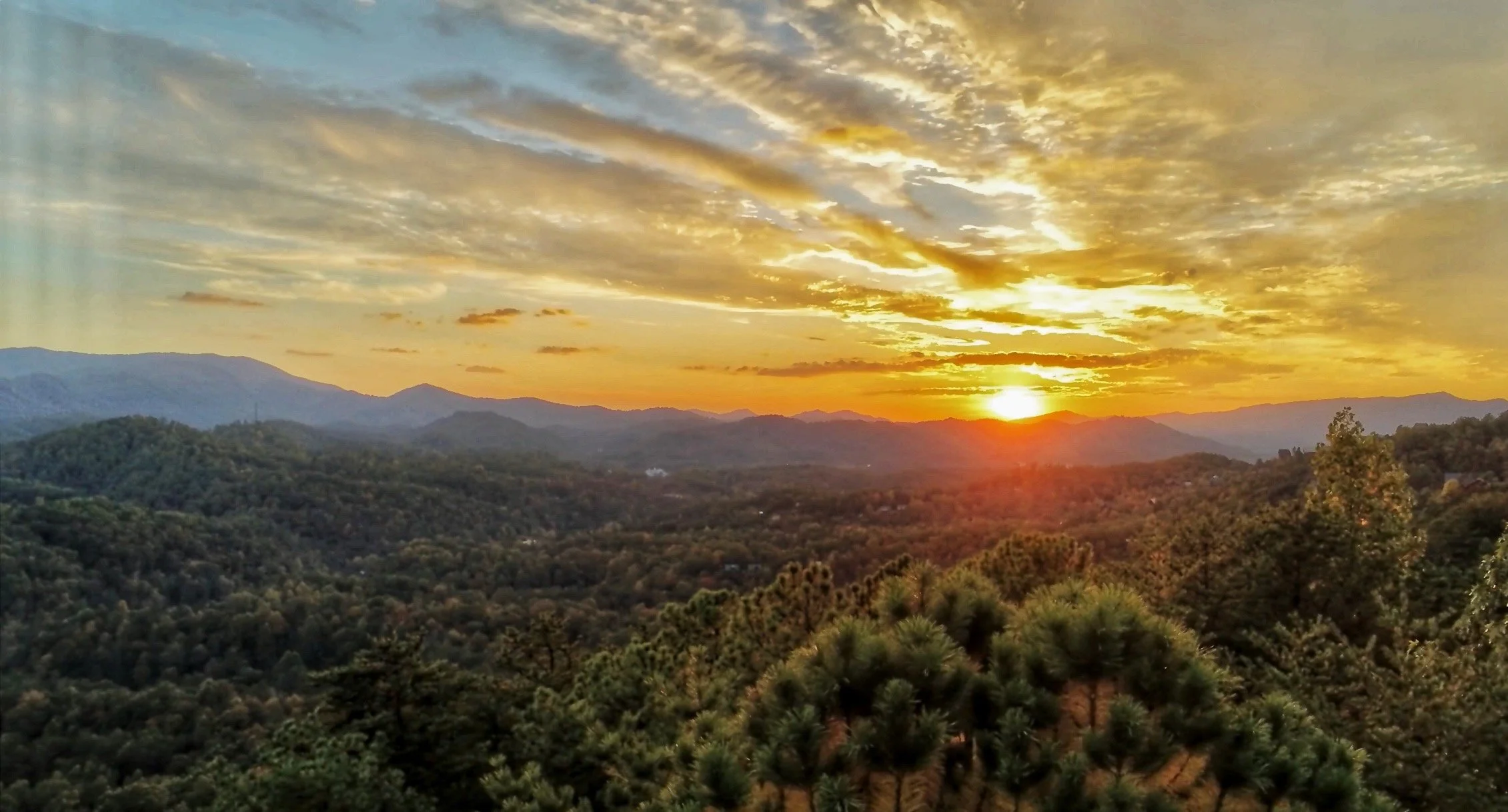 A scenic sunset over a mountainous landscape with a cloudy sky.