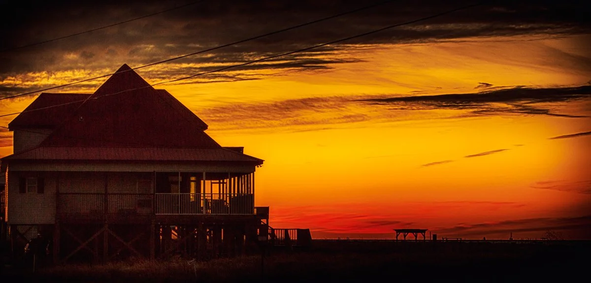 A house on stilts at sunset with a vibrant orange and yellow sky.