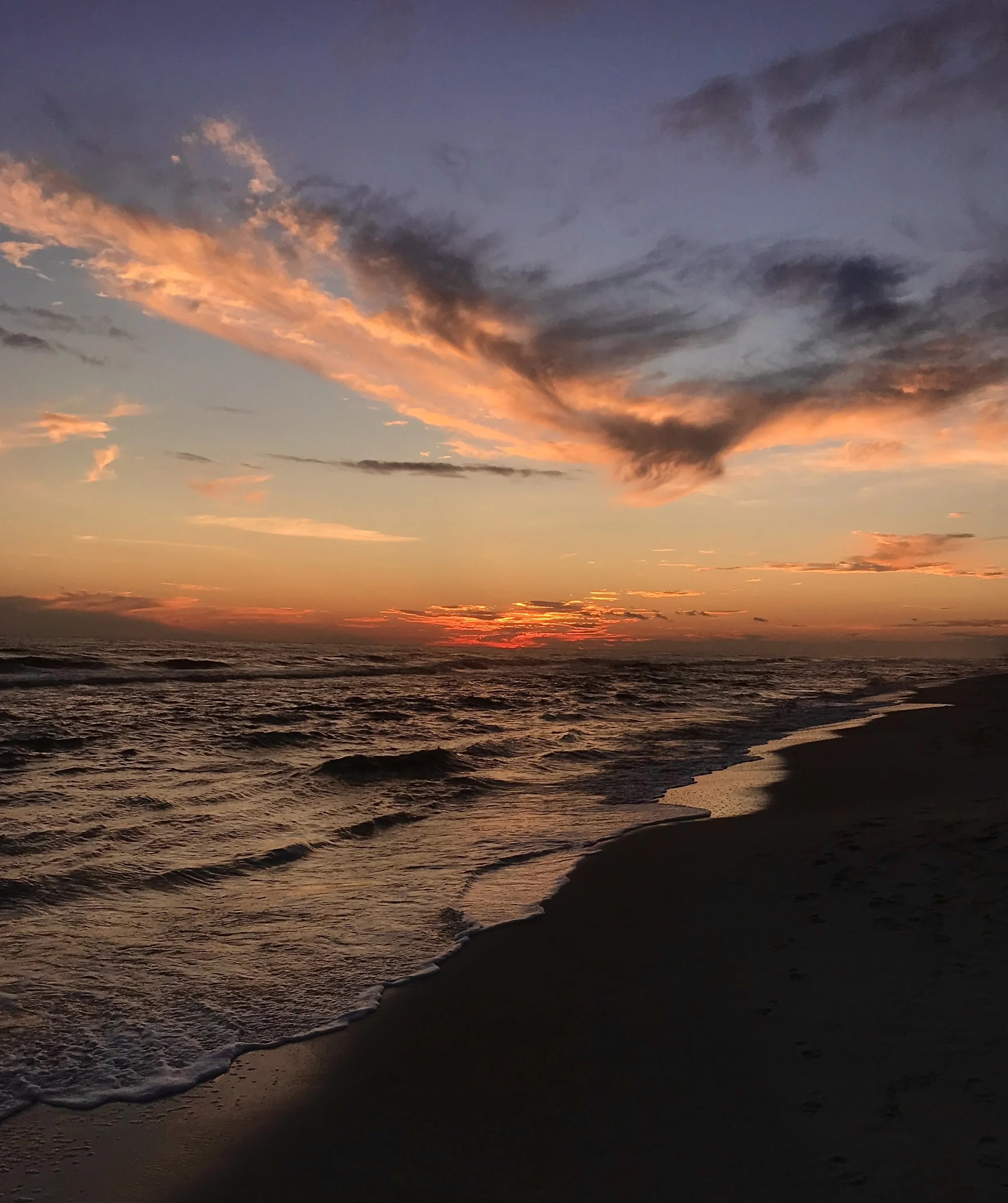 Sunset over the ocean with colorful clouds in the sky and gentle waves on the shoreline.
