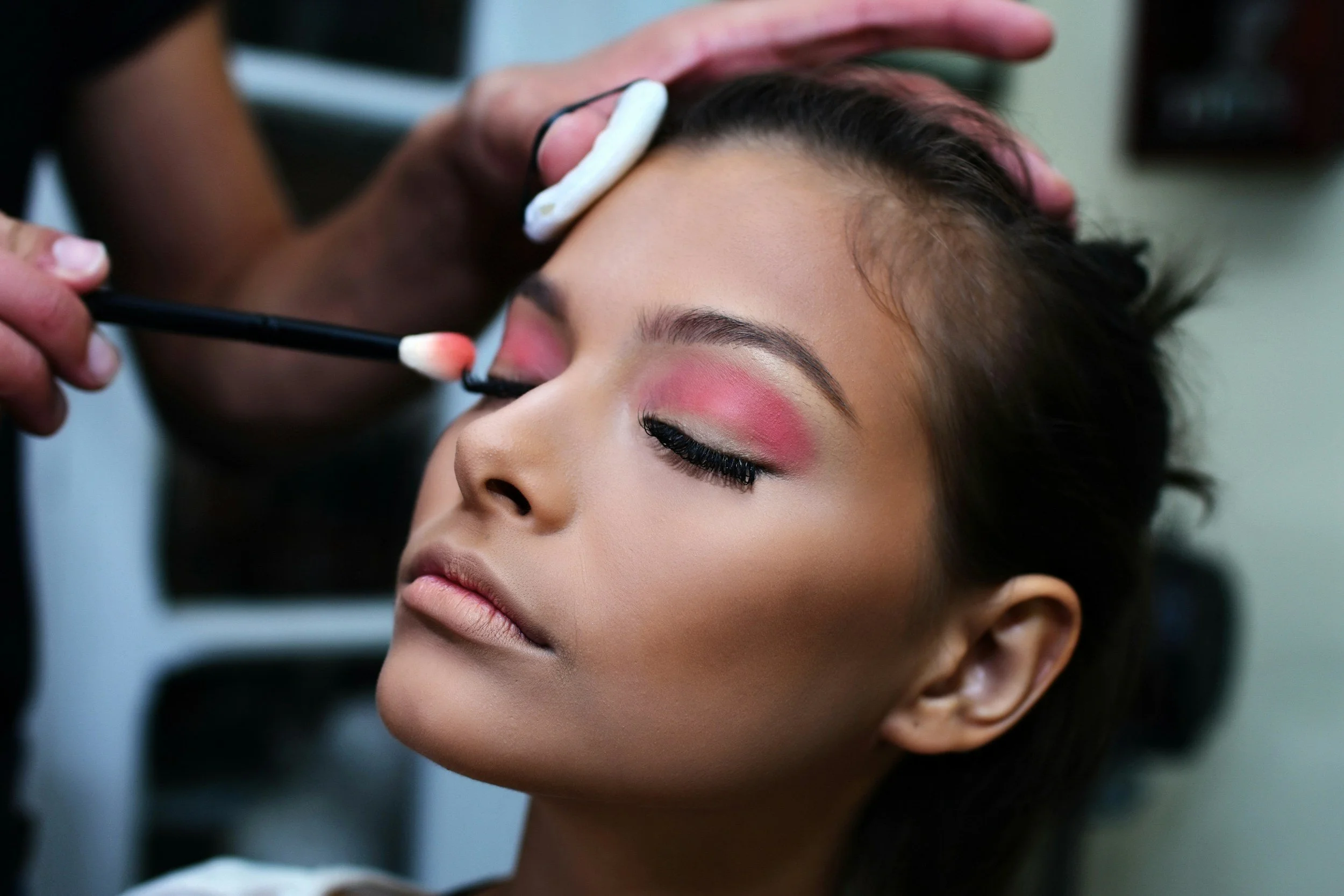 Makeup artist applying blush to a woman's cheeks with a brush.