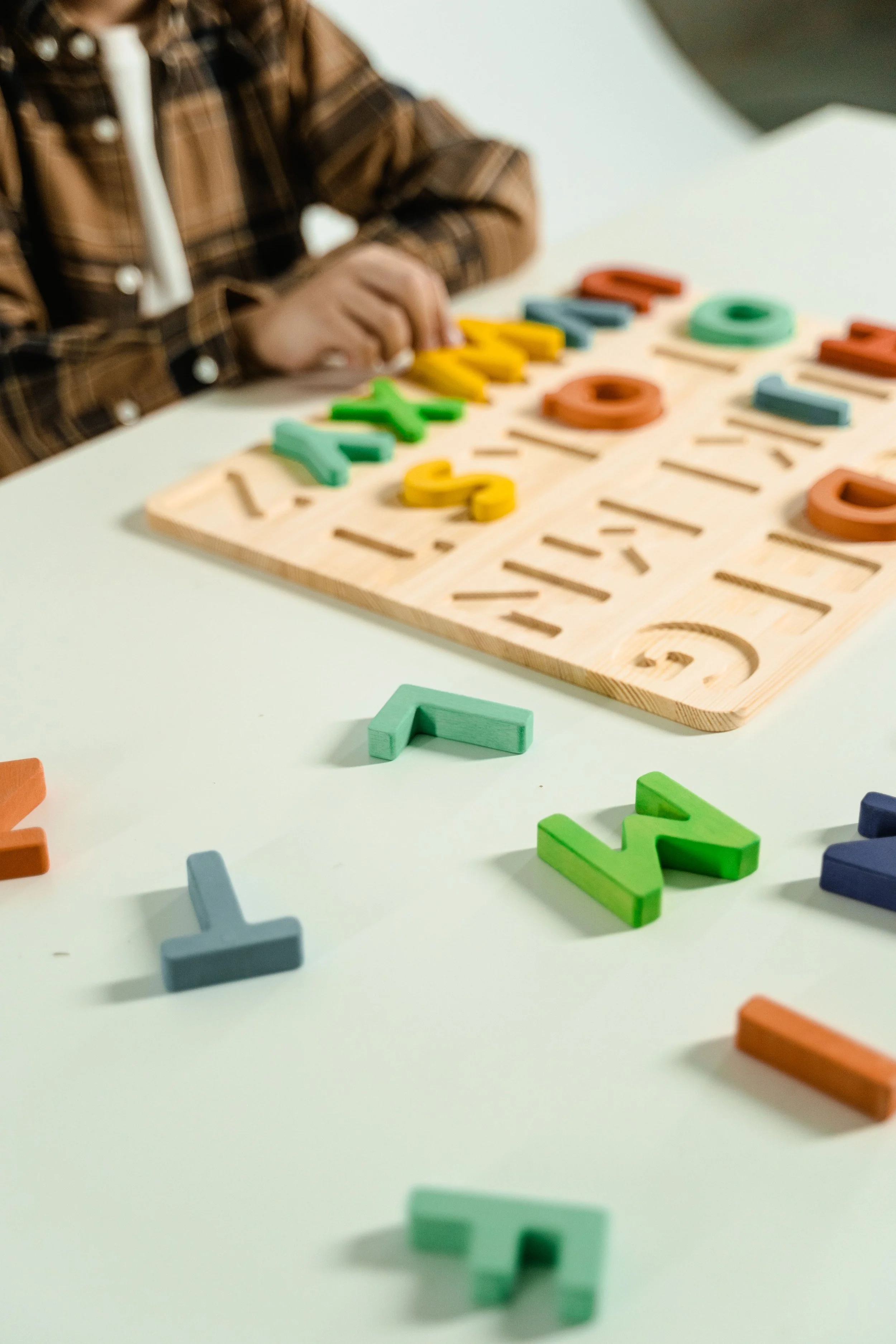 Child playing with colorful wooden alphabet letter toys on a white table.