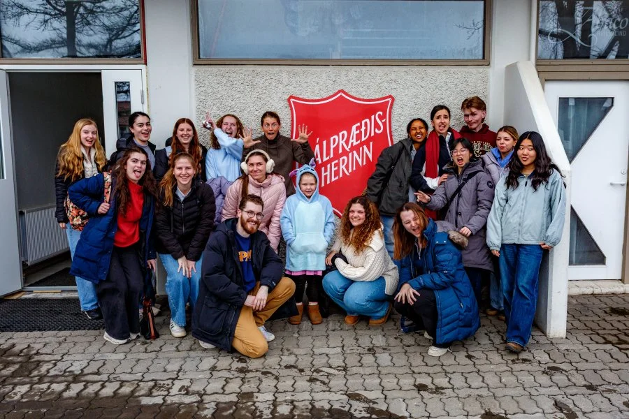 Group of teenagers and young adults posing outside a building with a red shield-shaped sign that reads 'Salvation Army' om Oce;amdoc.