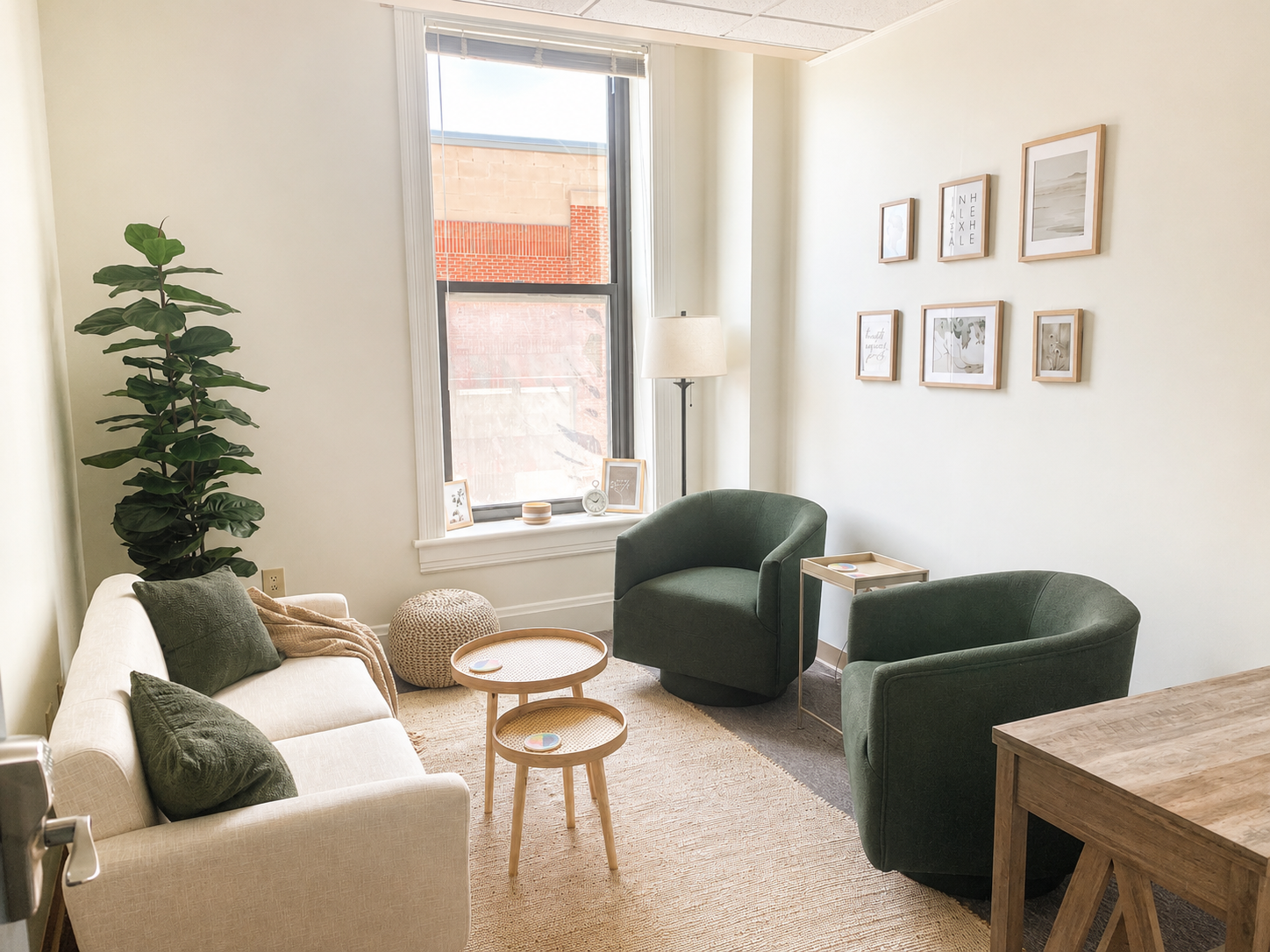 Living room with beige sofa, two green armchairs, a wicker pouf, a floor lamp, wall art, and a window with blinds, decorated in neutral tones and green accents.