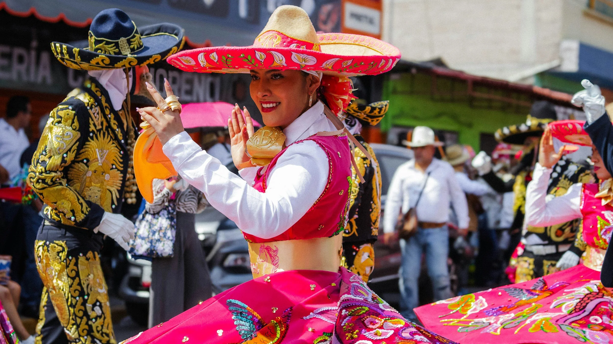 Mexican woman in traditional dress and large sombrero dancing with people in traditional fiesta clothes in the background