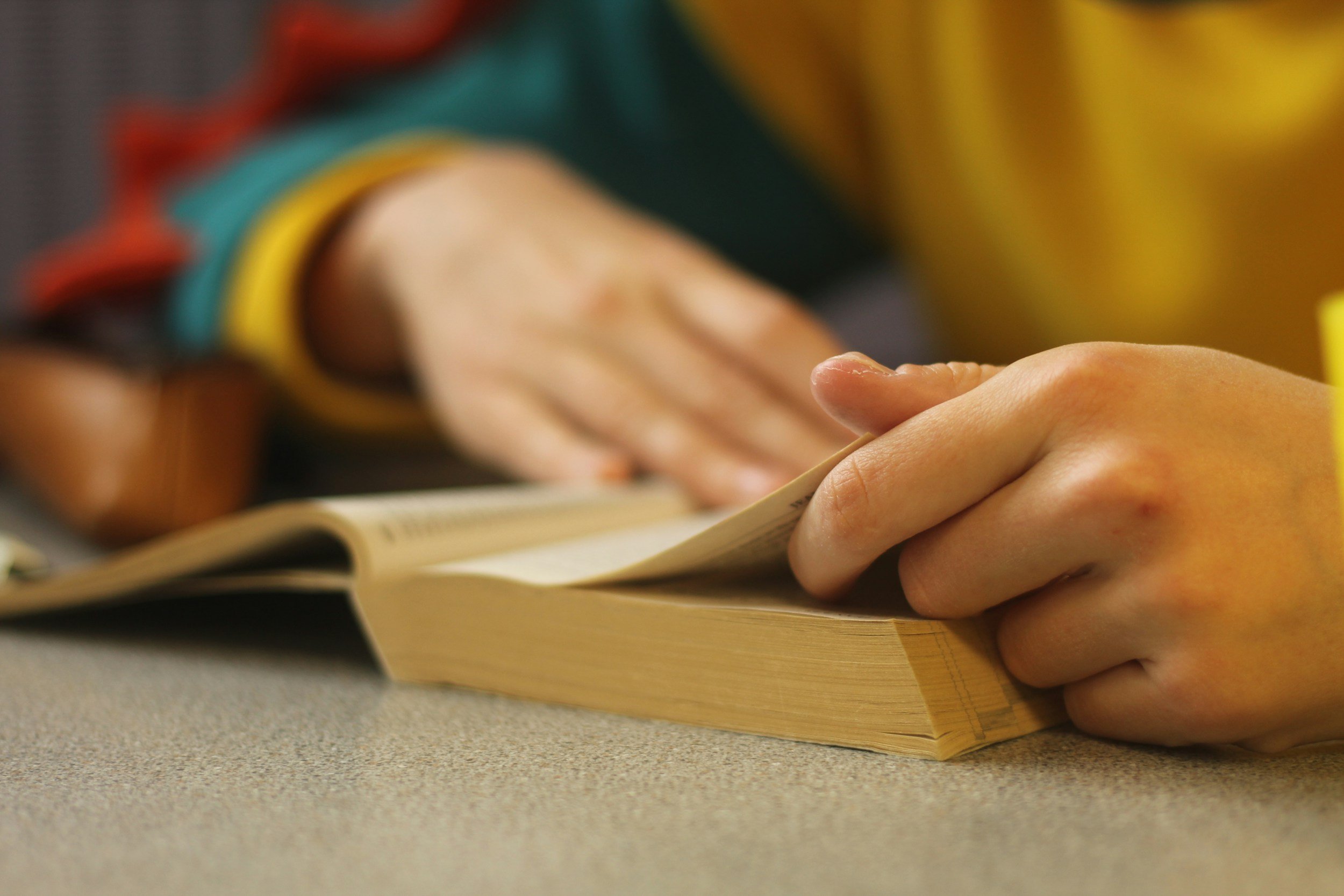 Close-up of a person's hand writing in a notebook on a desk, wearing a colorful striped sweater.