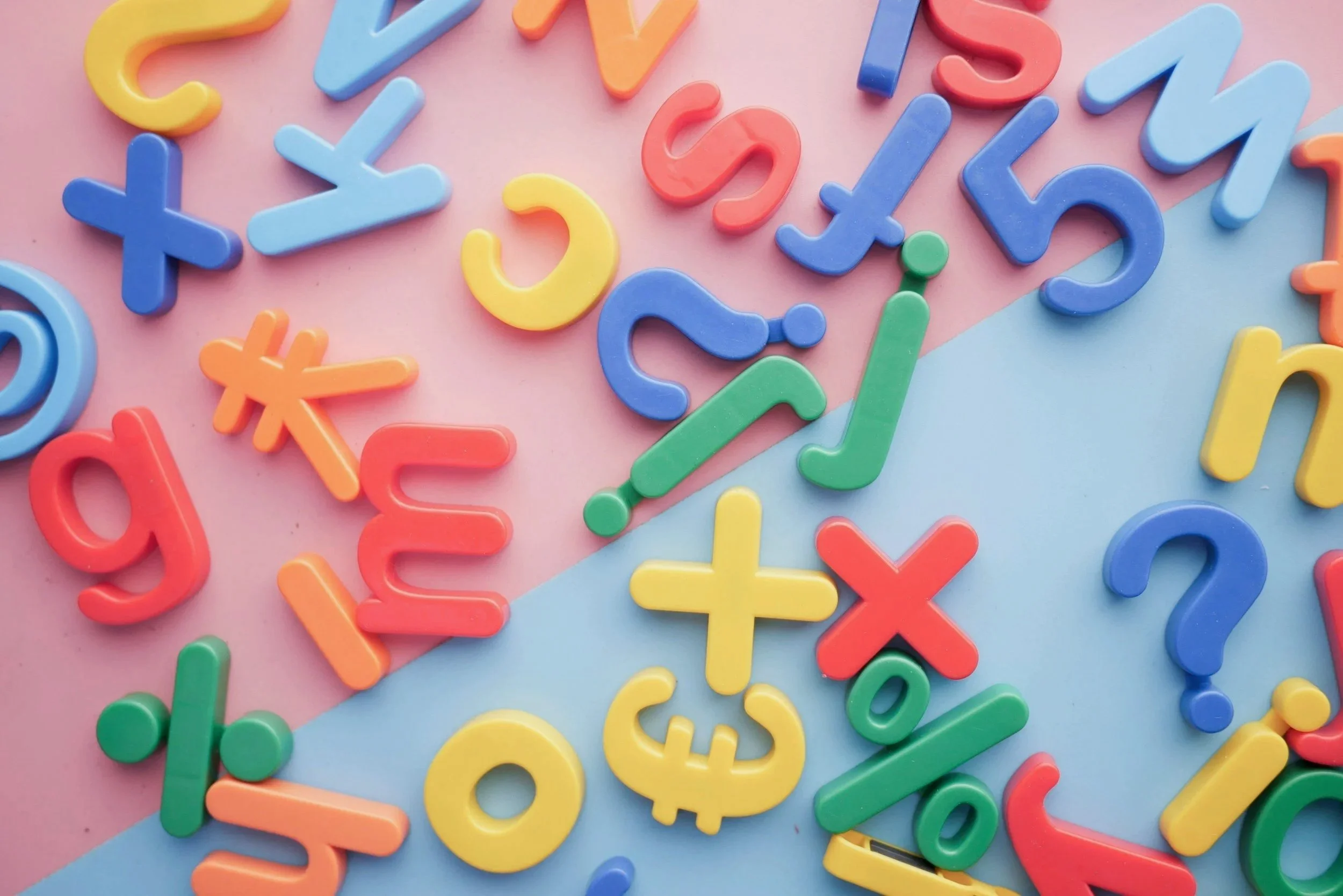 Colorful plastic alphabet letters scattered on pastel pink and blue backgrounds.