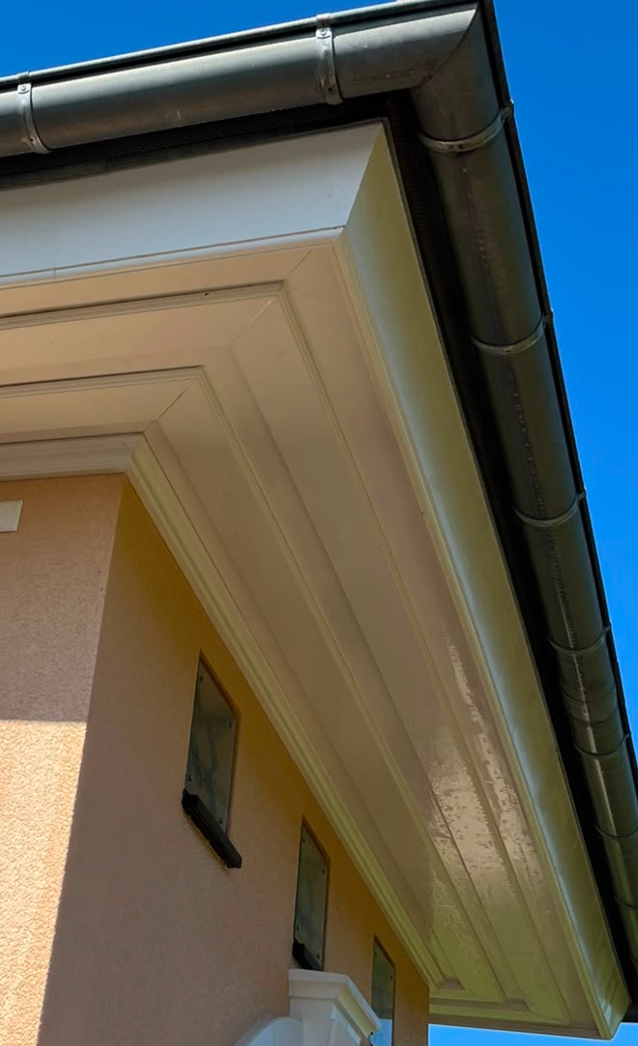 Ansicht eines Gebäudes mit einer Dachrinne und drei kleine Fenster, die an der gelben Wand angebracht sind, bei sonnigem Wetter.