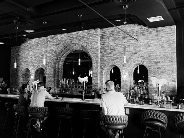 People sitting at a bar with brick walls, arched openings, and pendant lighting