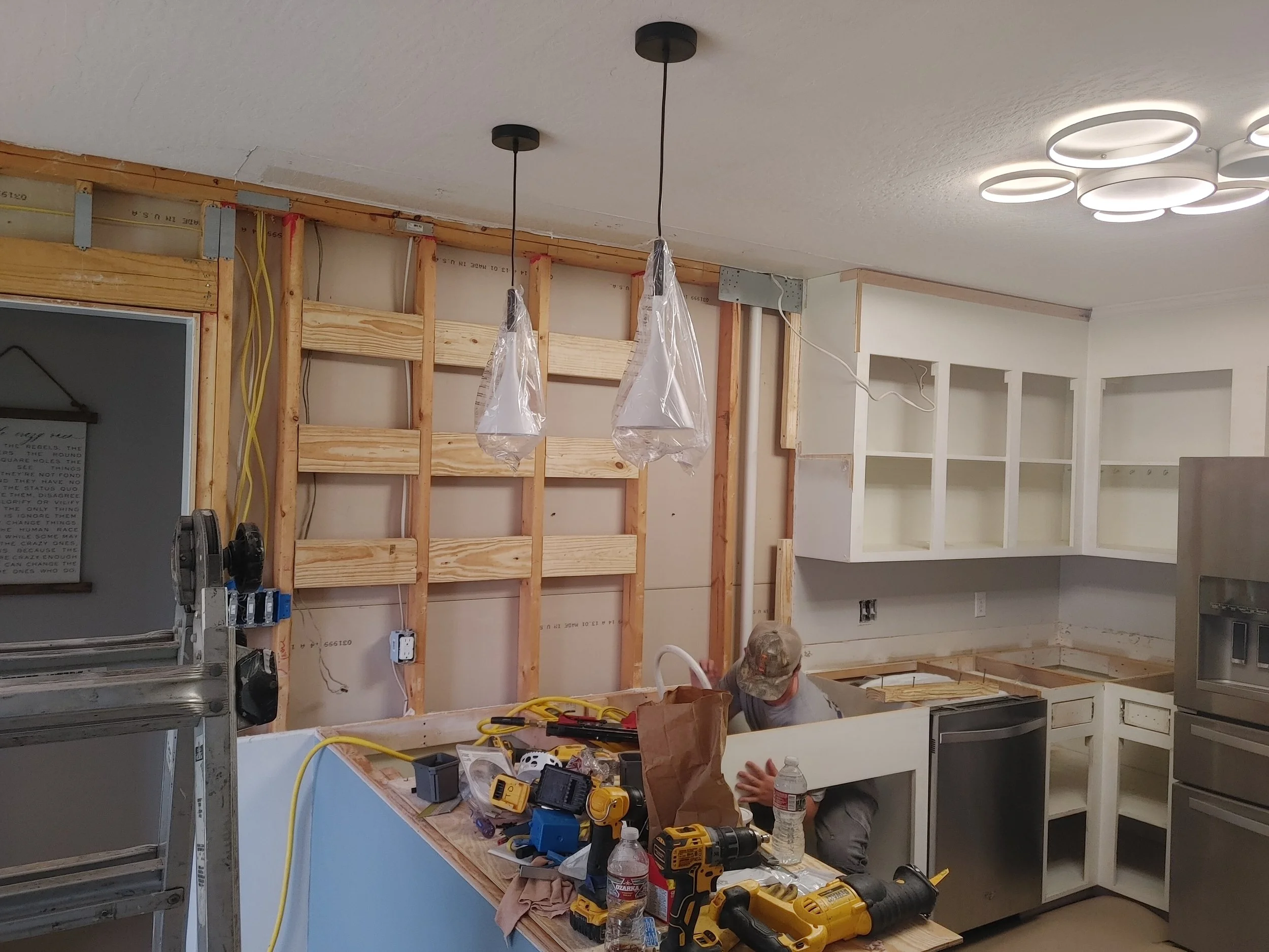 Construction workers installing kitchen cabinets and fixtures, with tools and materials on a workbench.