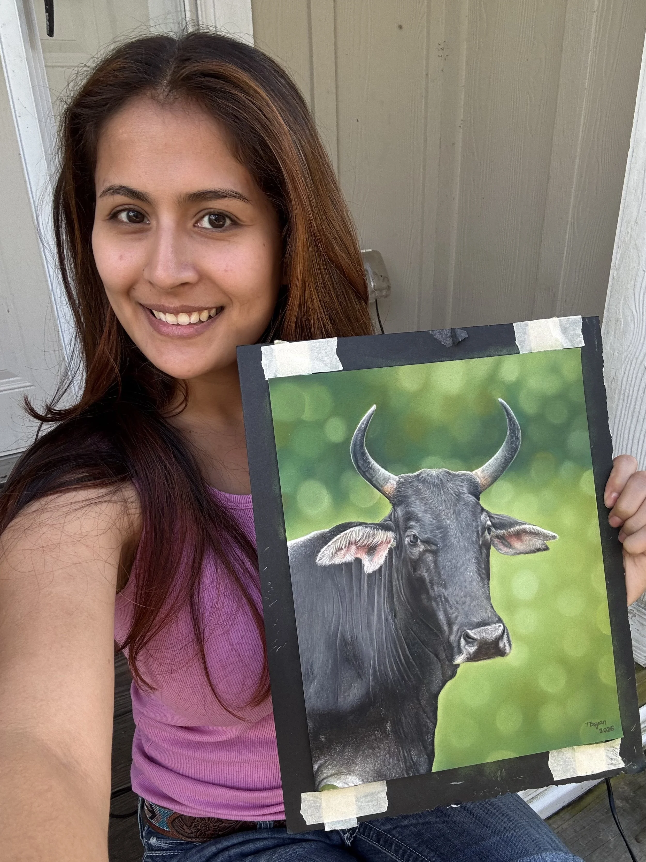 A woman with long brown hair and a pink tank top smiling while holding a painting of a buffalo with green background.